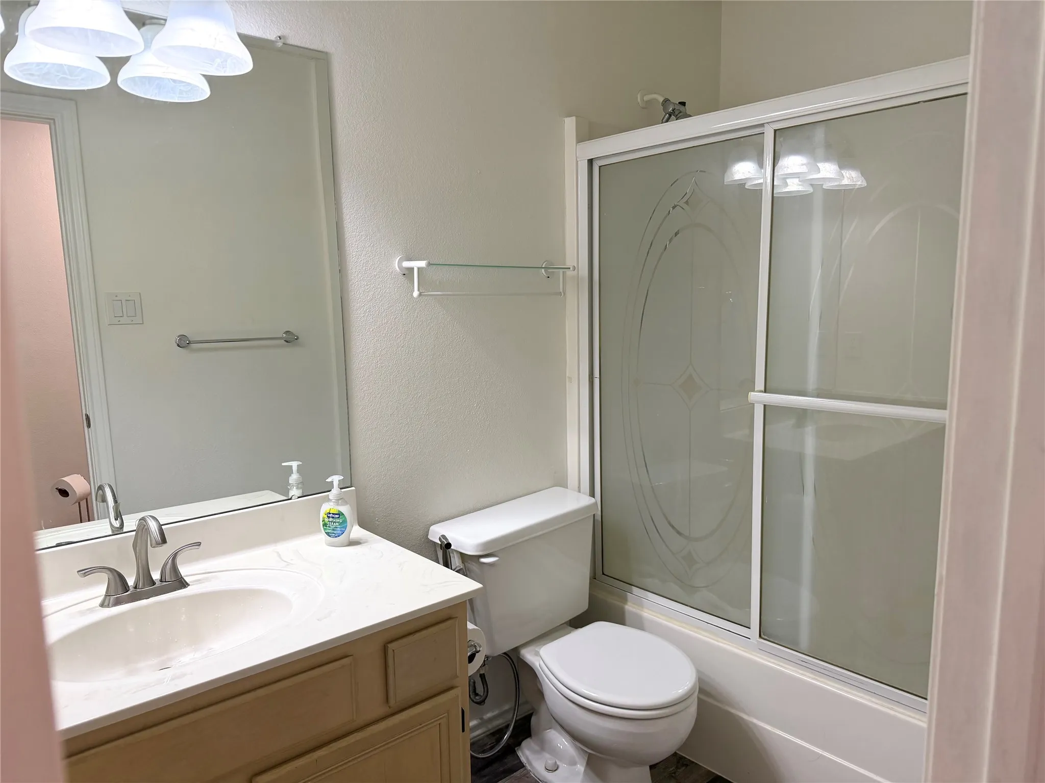 Bathroom featuring a light-colored vanity with an integrated sink, a large wall mirror, and a combination shower/tub with frosted sliding glass doors