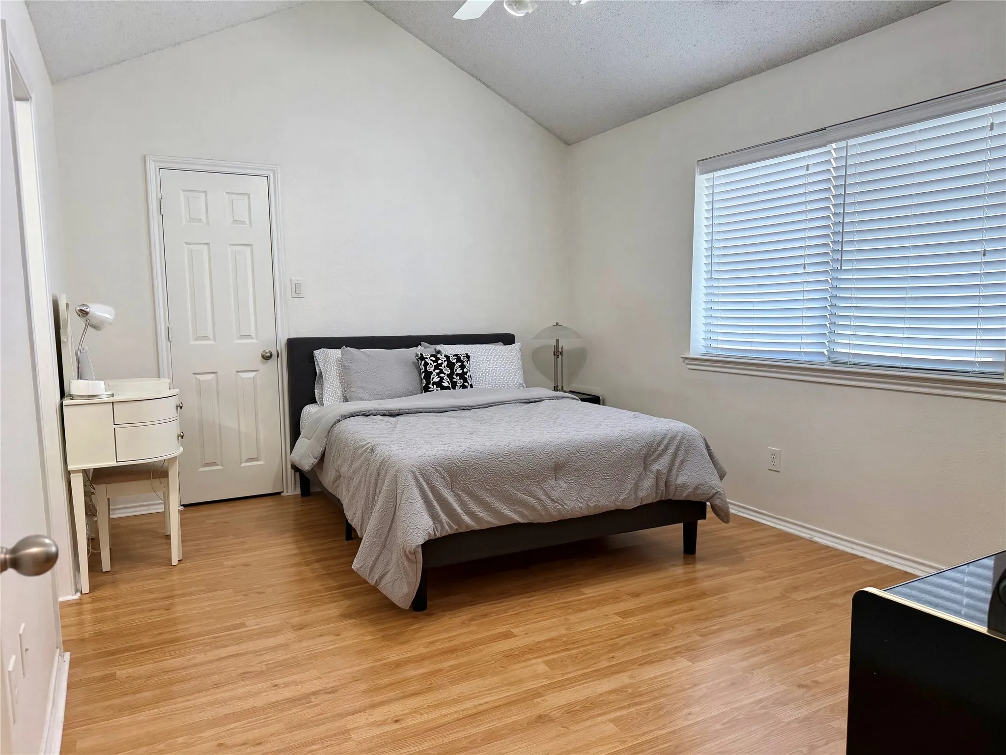 Spacious room featuring vaulted ceilings, wood-finish flooring, and a large window with horizontal blinds