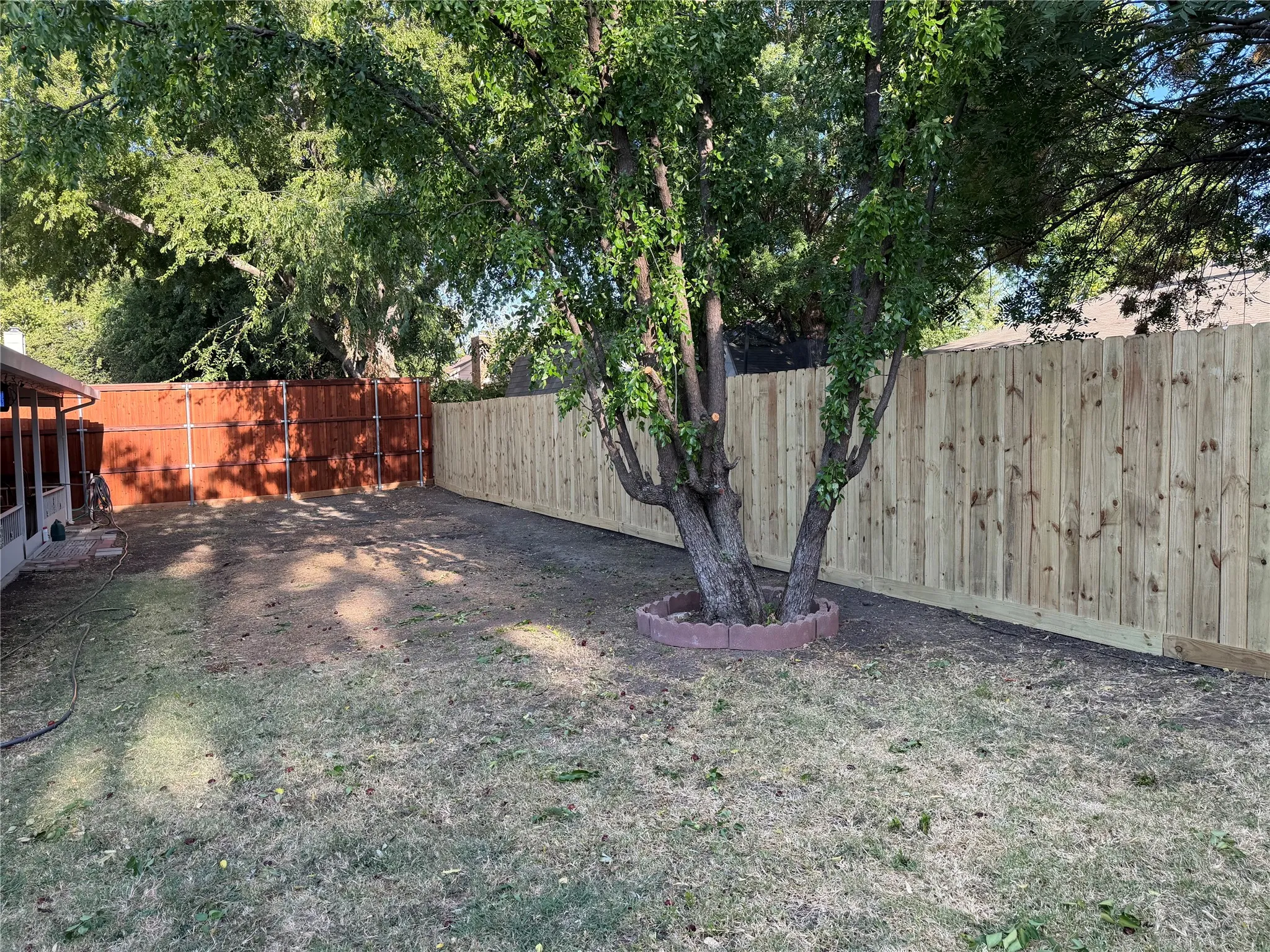 Spacious backyard with a wood privacy fence, mature trees, and a tree ring