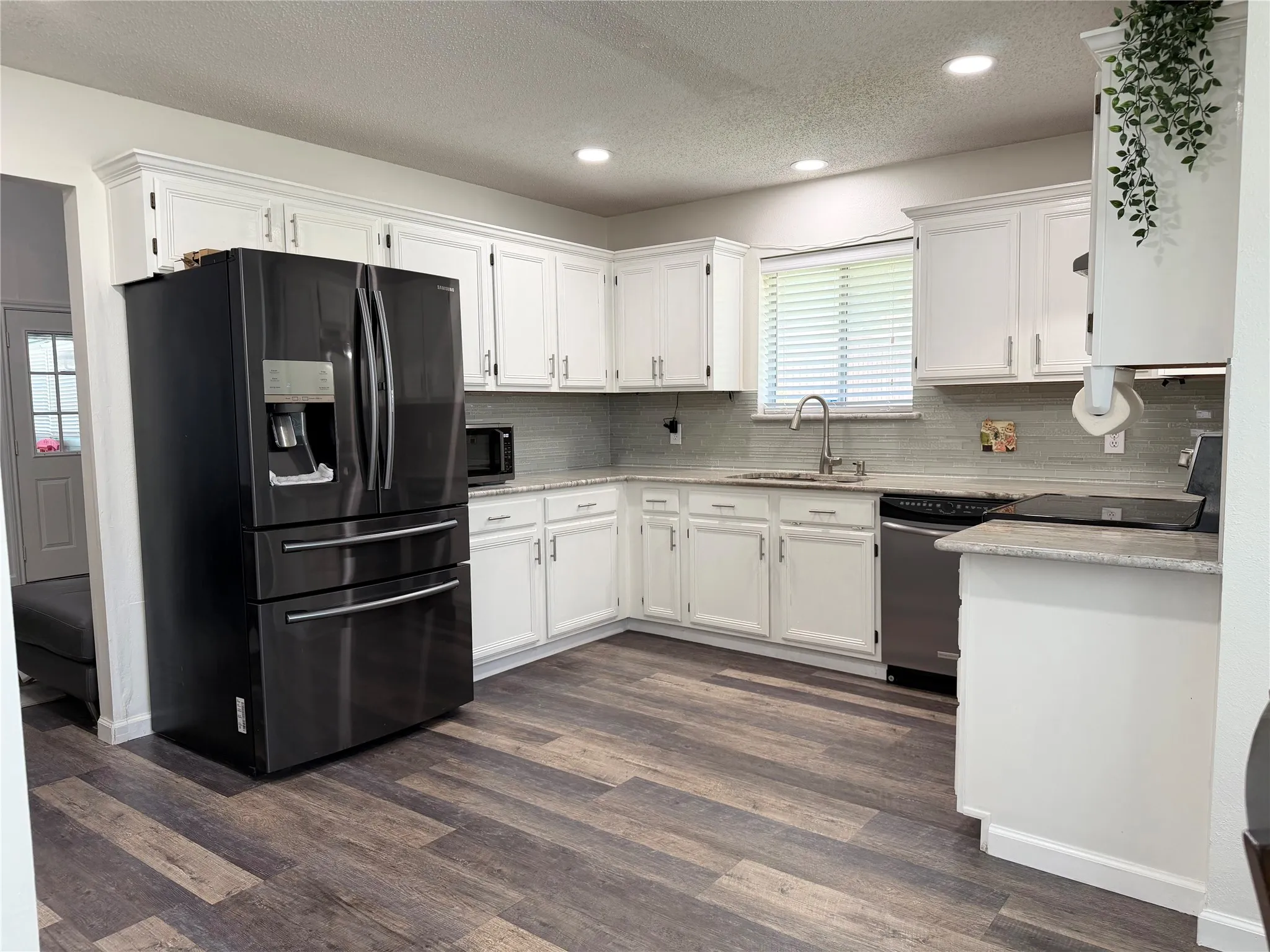 Modern kitchen featuring white cabinetry, light-toned countertops, a glass tile backsplash, and dark wood-finish flooring