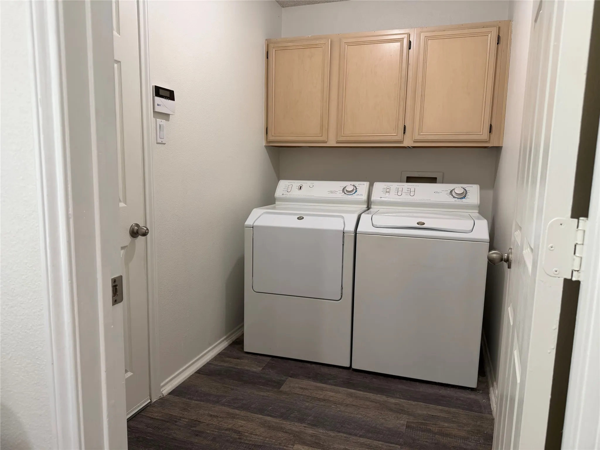 Dedicated laundry area featuring wood-finish flooring, light-toned upper cabinetry, and white appliances