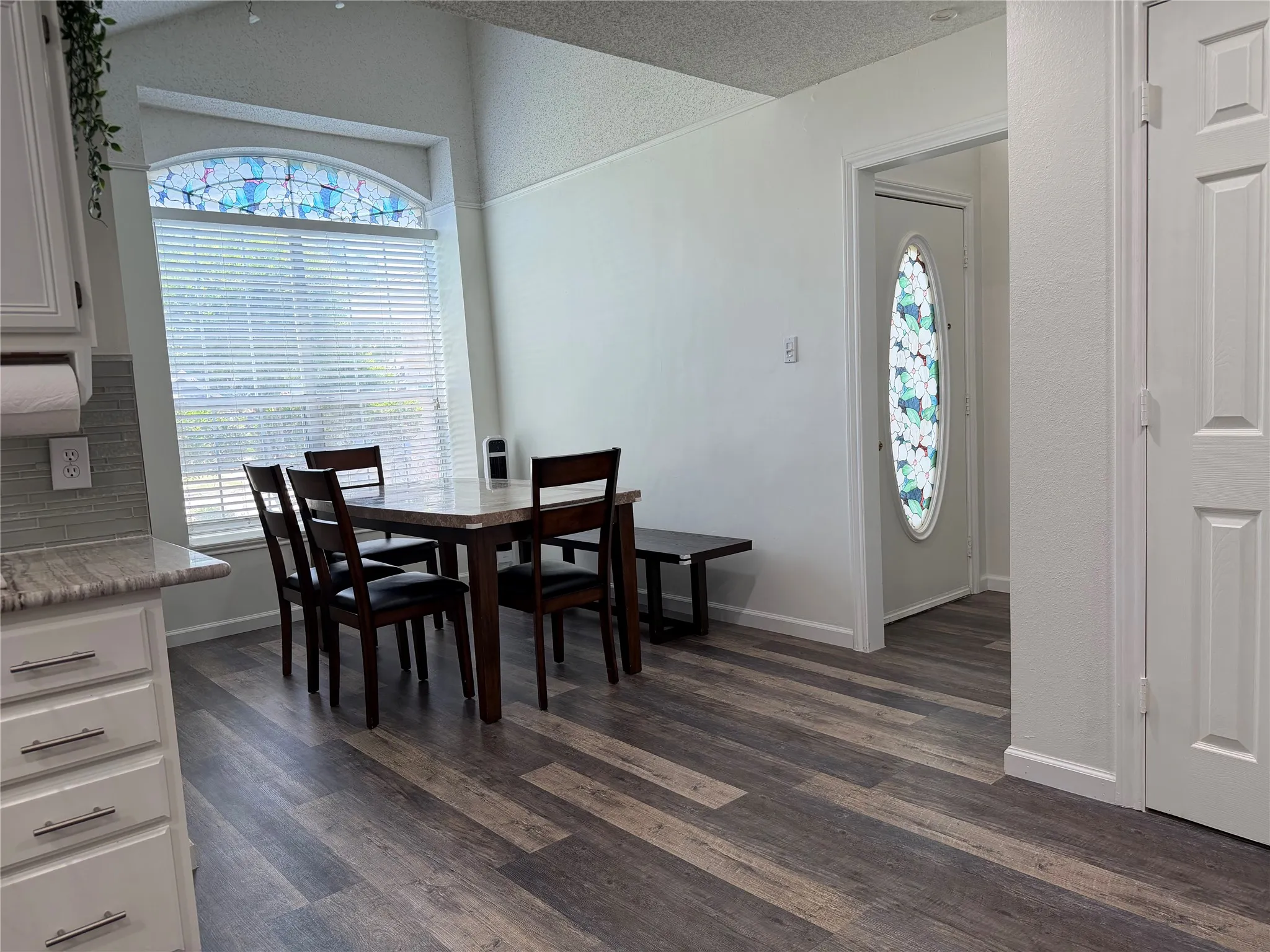 Dining area featuring wood-finish flooring, a large window with an arched stained-glass transom, and a paneled entry door with an oval stained-glass insert
