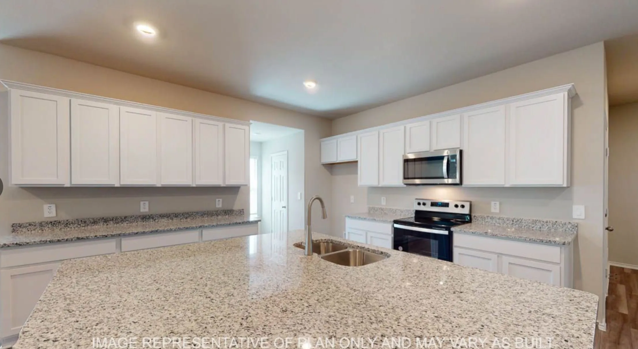 Kitchen featuring an expansive island with a dual basin stainless steel sink, light-toned granite countertops, white shaker cabinetry, stainless steel microwave, and built-in electric range