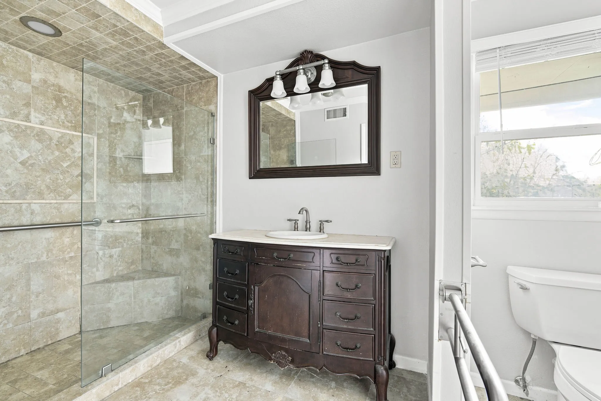Bathroom featuring a glass-enclosed shower with tile surround, a built-in shower bench, and grab bars