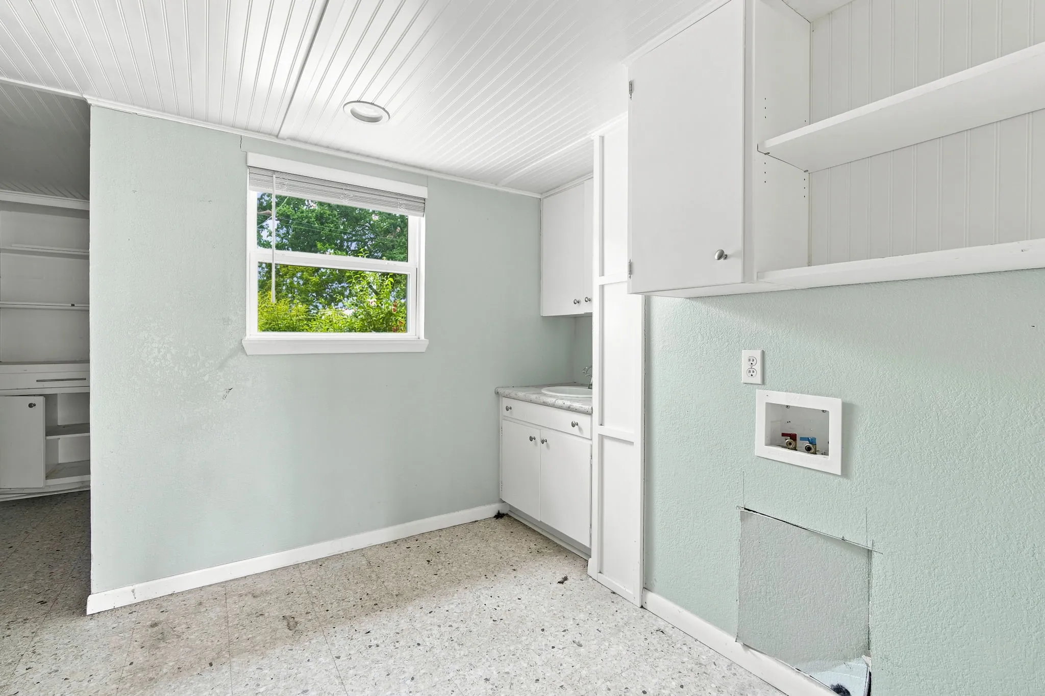 Utility room featuring white beadboard ceiling and walls, white cabinetry, a built-in sink, and a window