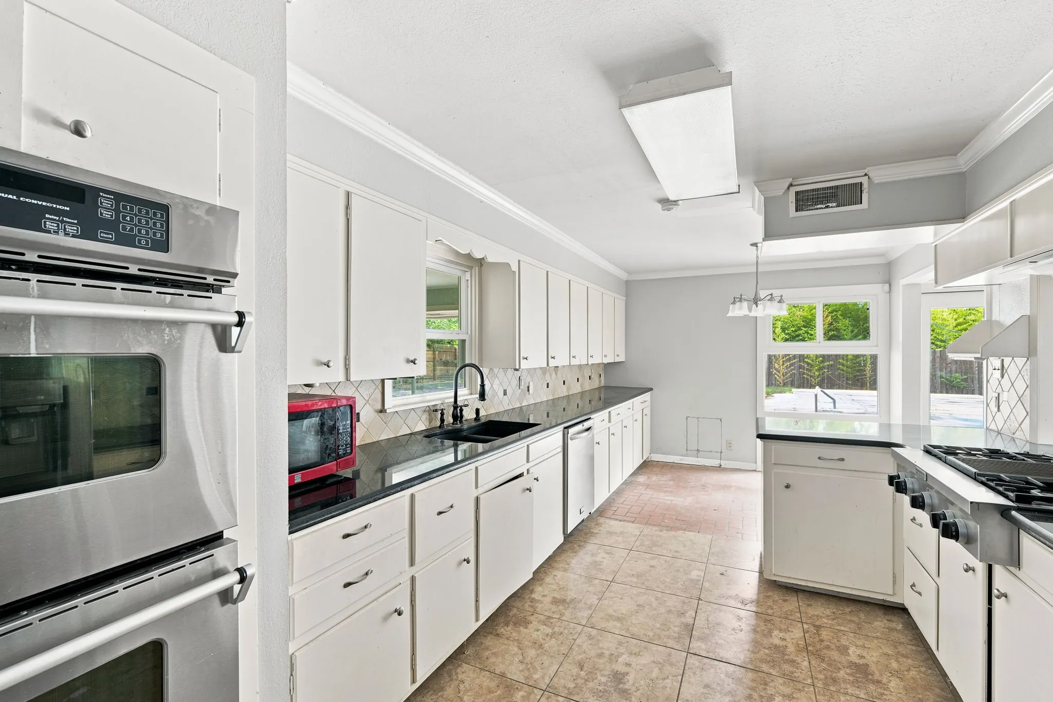 Kitchen featuring white cabinetry, black countertops, stainless steel double wall ovens, a black faucet, and tile flooring