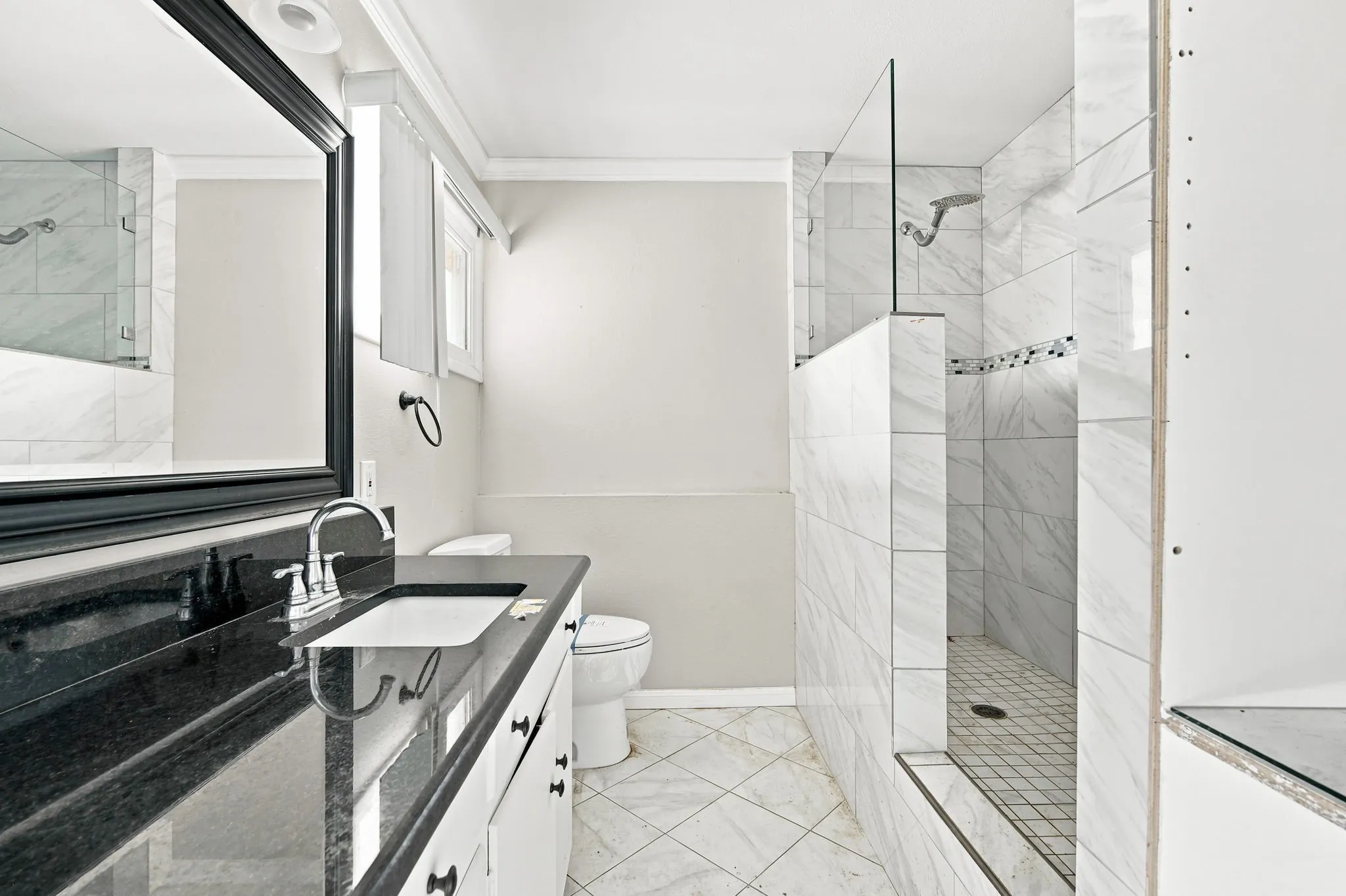 Bathroom featuring a dark countertop vanity with an undermount sink and chrome faucet, a large framed mirror, and a walk-in shower with glass partition and tiled walls