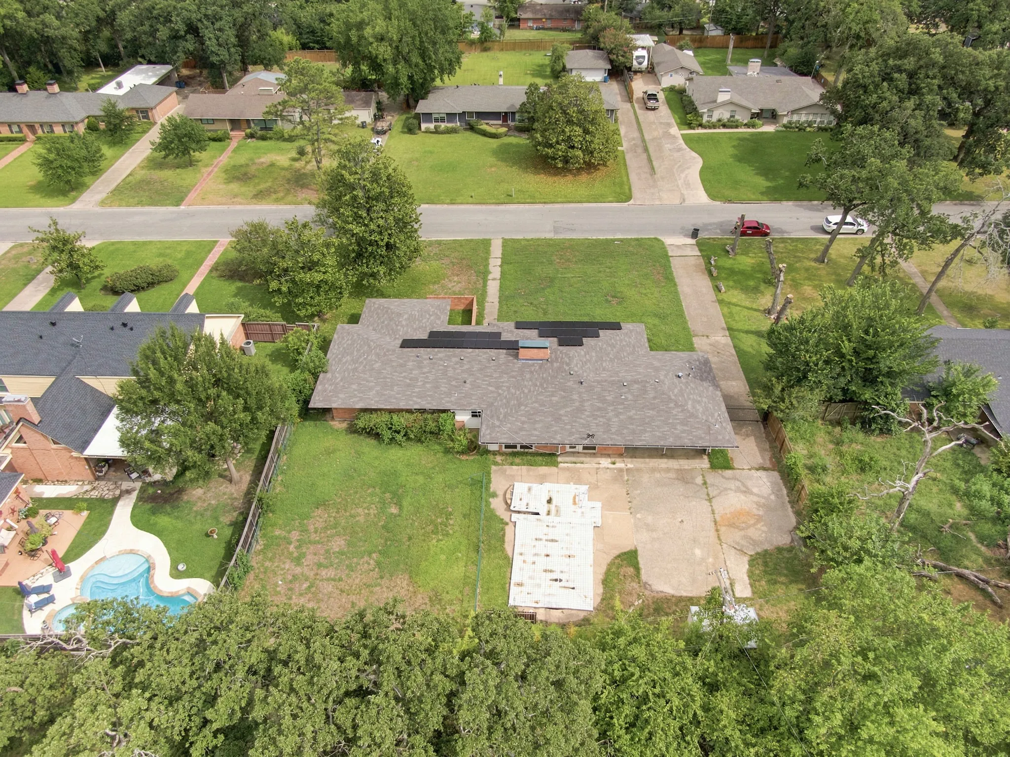 Expansive property featuring a mature tree line, a paved driveway, and a shingle roof