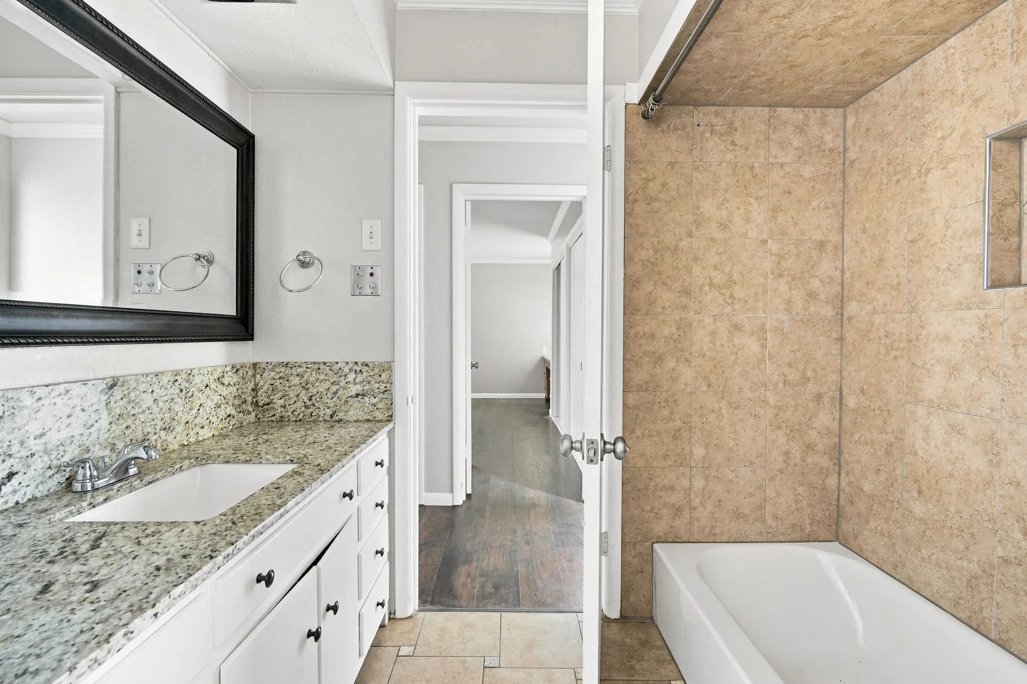 Bathroom featuring a granite vanity with an undermount sink, white cabinetry, and a framed mirror