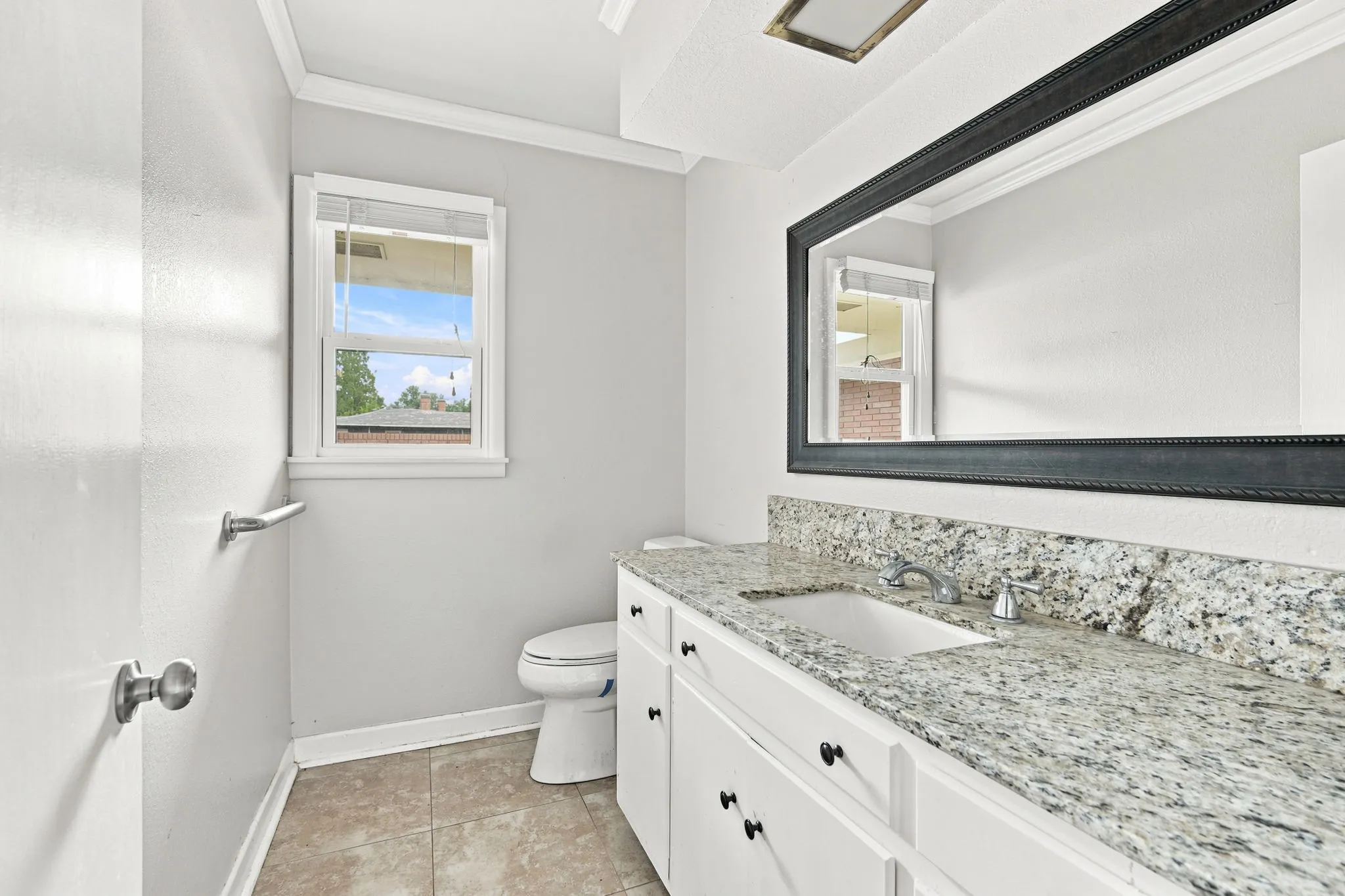 Bathroom featuring a white vanity with granite-style countertop, undermount sink, and dark framed mirror