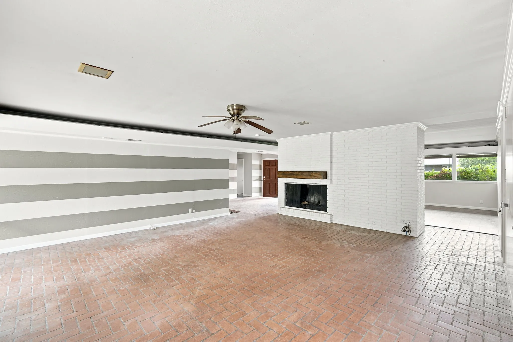 Spacious room featuring brick flooring, a white brick fireplace with a wood mantle, and a ceiling fan
