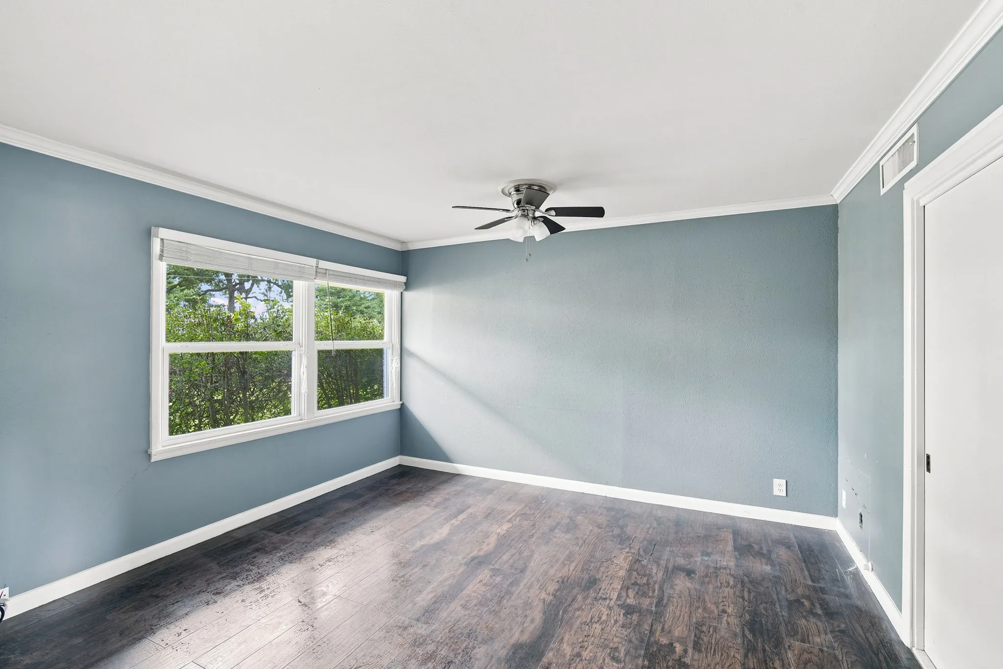 Interior room featuring a large window, dark wood-finish flooring, light blue walls, and a ceiling fan with integrated lighting