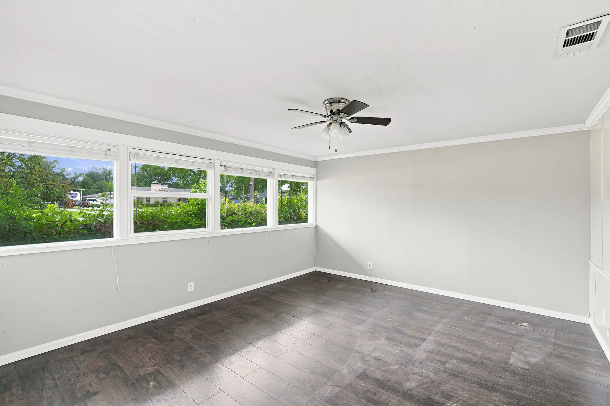 Spacious room featuring multiple large windows, dark wood-finish flooring, a ceiling fan with integrated lighting, and white baseboards