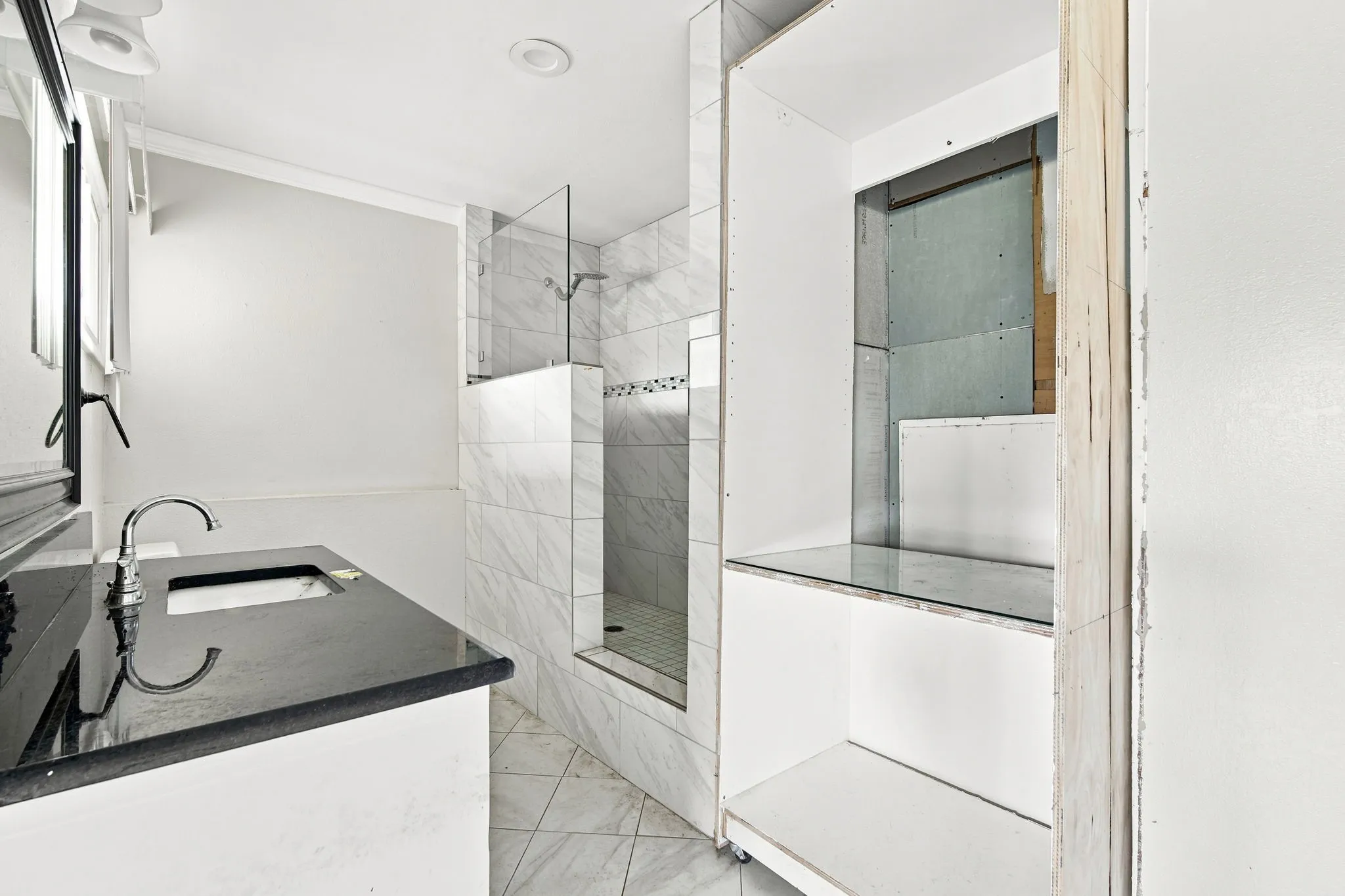 Bathroom featuring a dark countertop vanity with an undermount sink and chrome faucet, a walk-in shower with glass partition and white tiled walls, and a recessed ceiling light