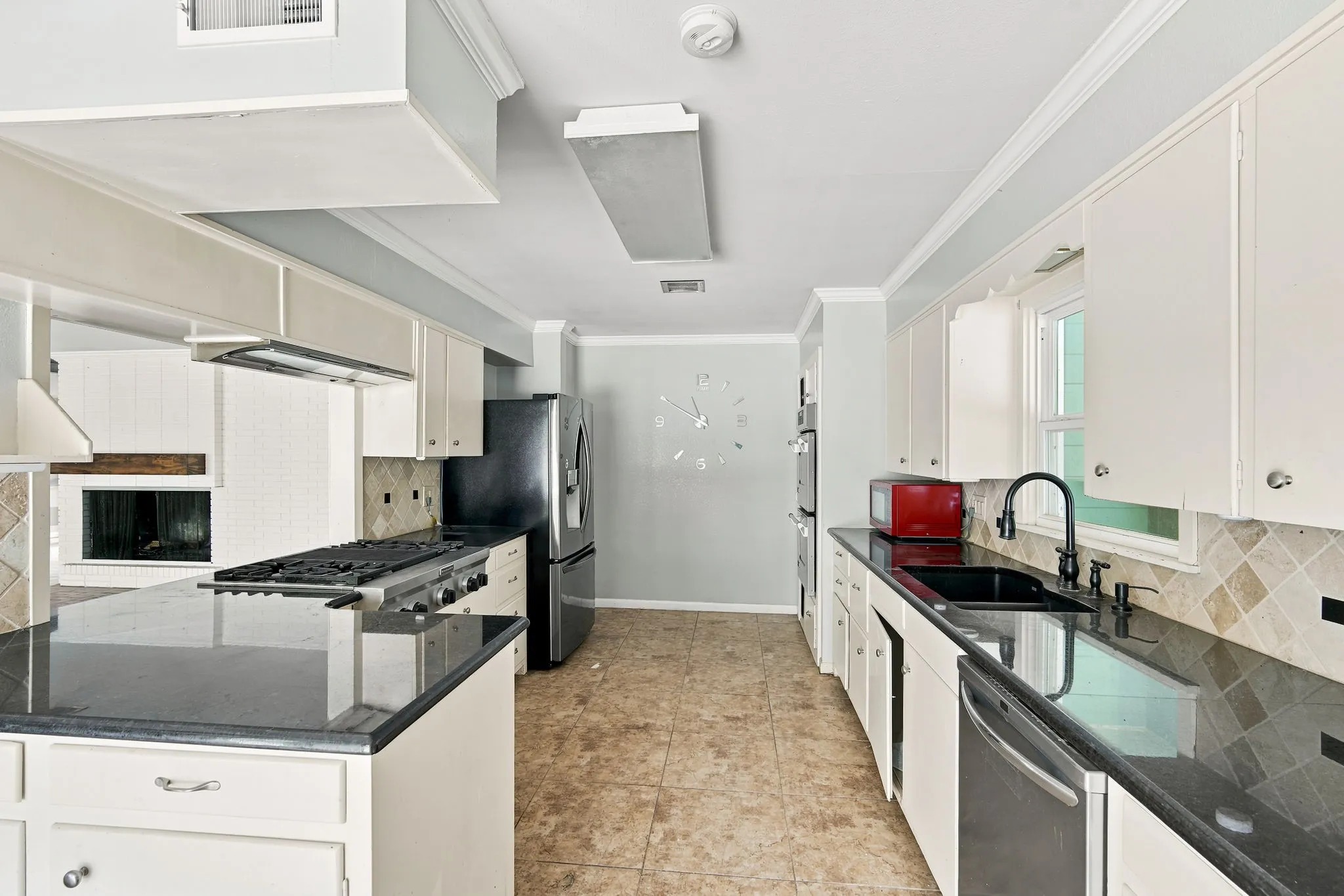 Galley kitchen featuring white cabinetry, dark countertops, a built-in gas range, tile flooring, and a black sink with a gooseneck faucet