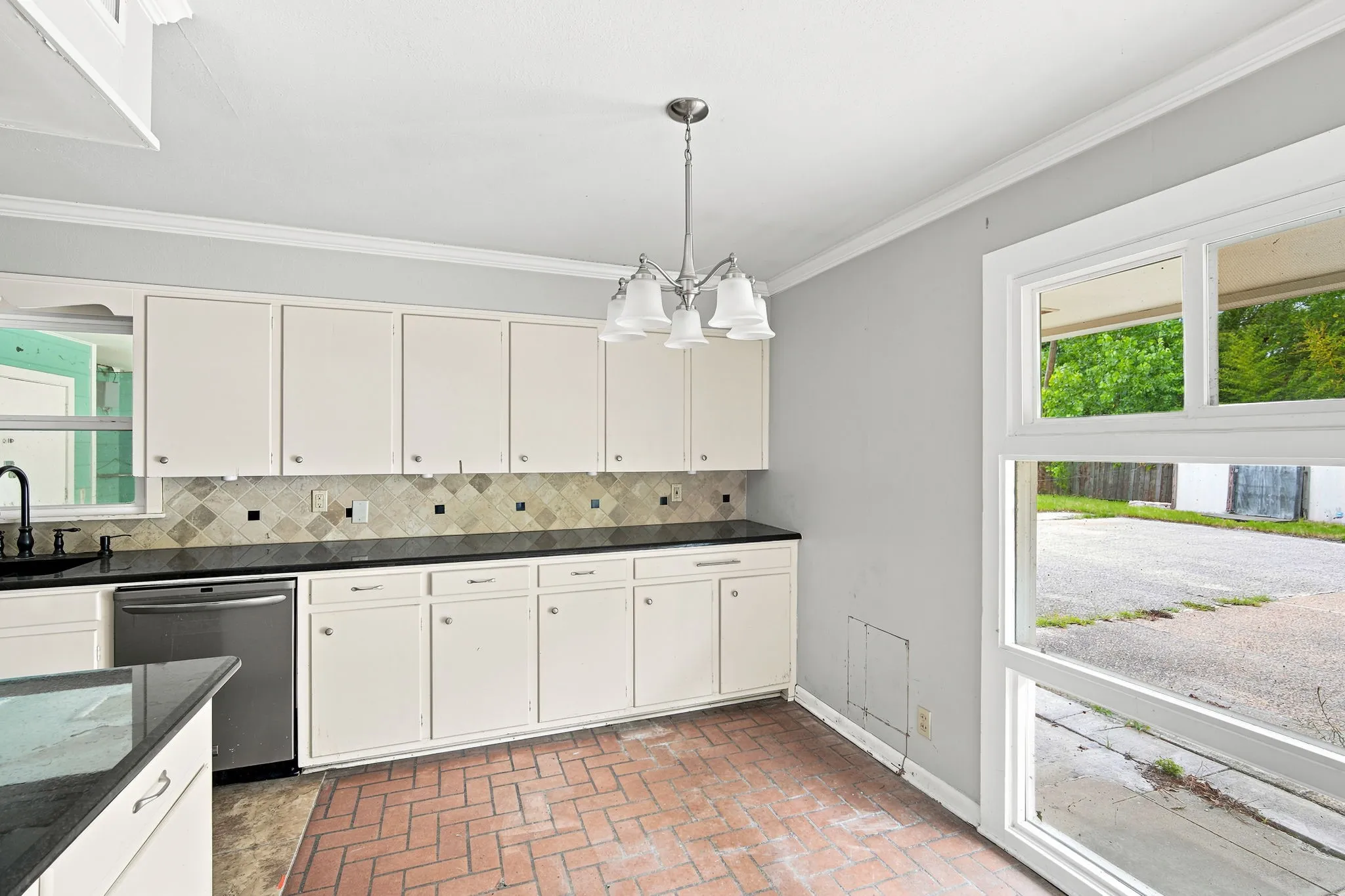 Kitchen featuring white cabinetry, dark countertops, a mosaic tile backsplash, stainless steel appliances, and brick-finish flooring