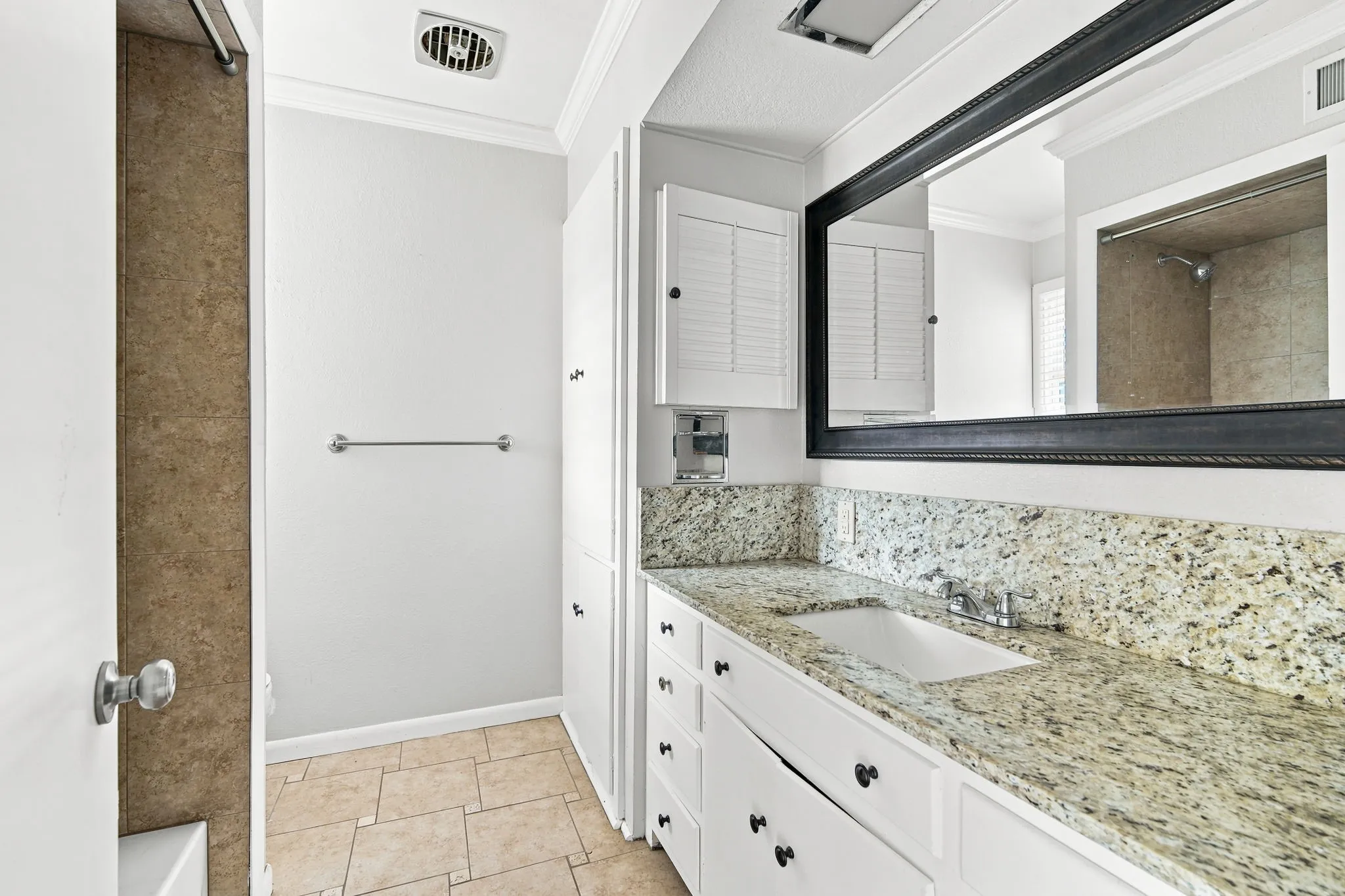 Bathroom vanity with a light-toned stone countertop, integrated sink, and white cabinetry with black hardware