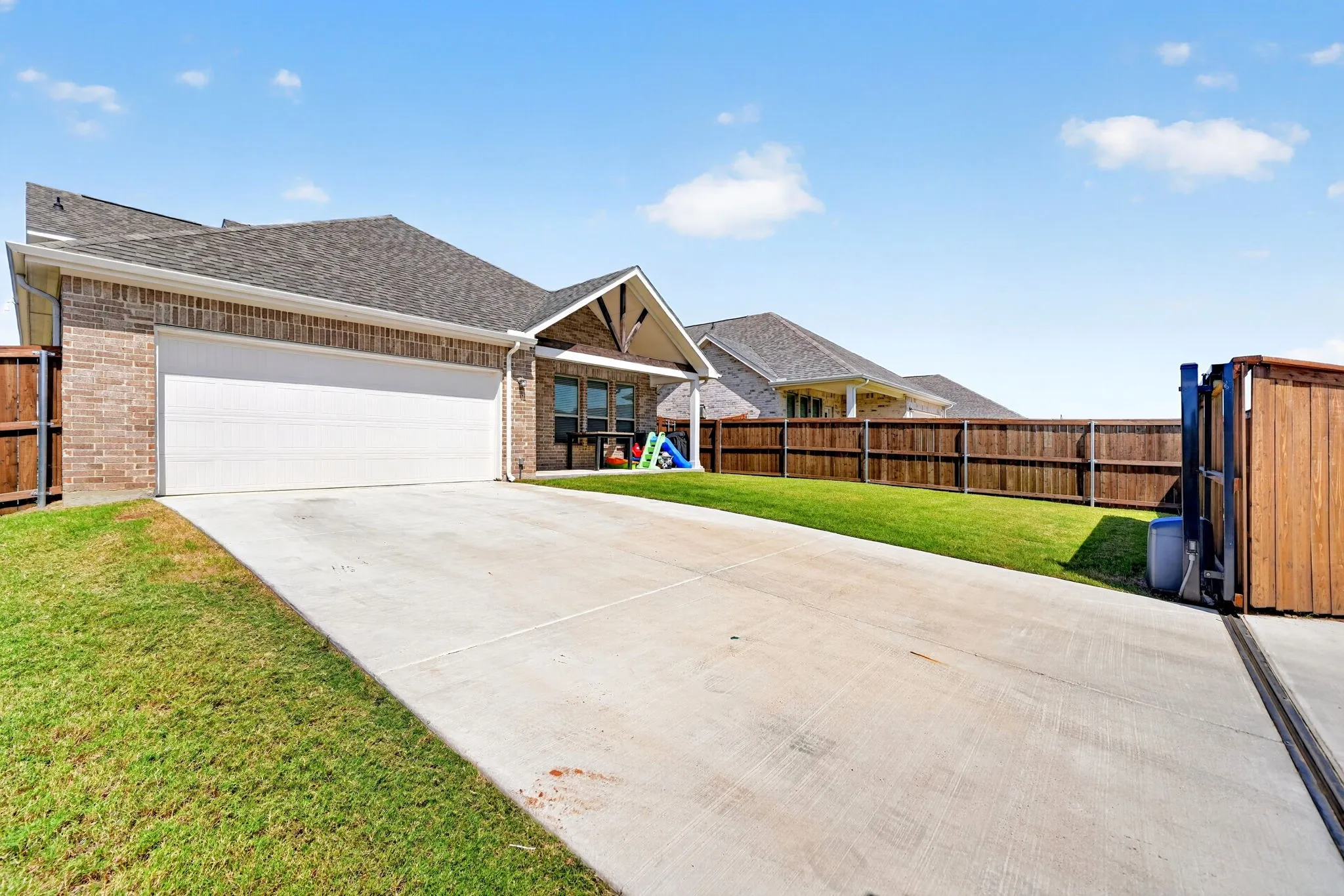 Brick exterior with a prominent two-car garage, concrete driveway, fenced yard, and a covered back patio