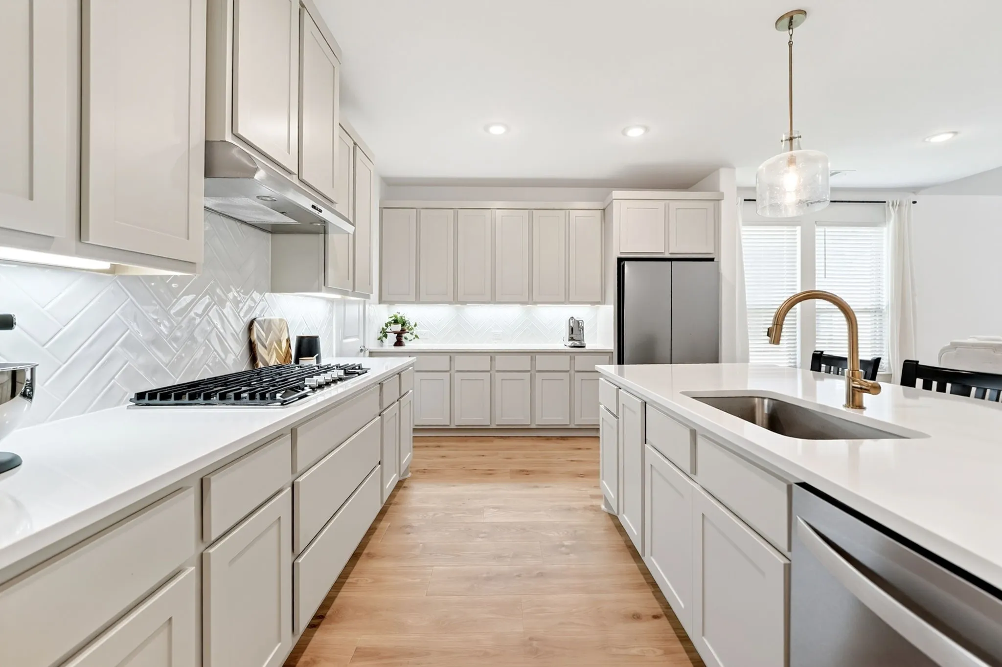 Kitchen featuring light-toned cabinetry, white countertops, wood-finish flooring, stainless steel appliances, and a central island with an undermount sink and gooseneck faucet