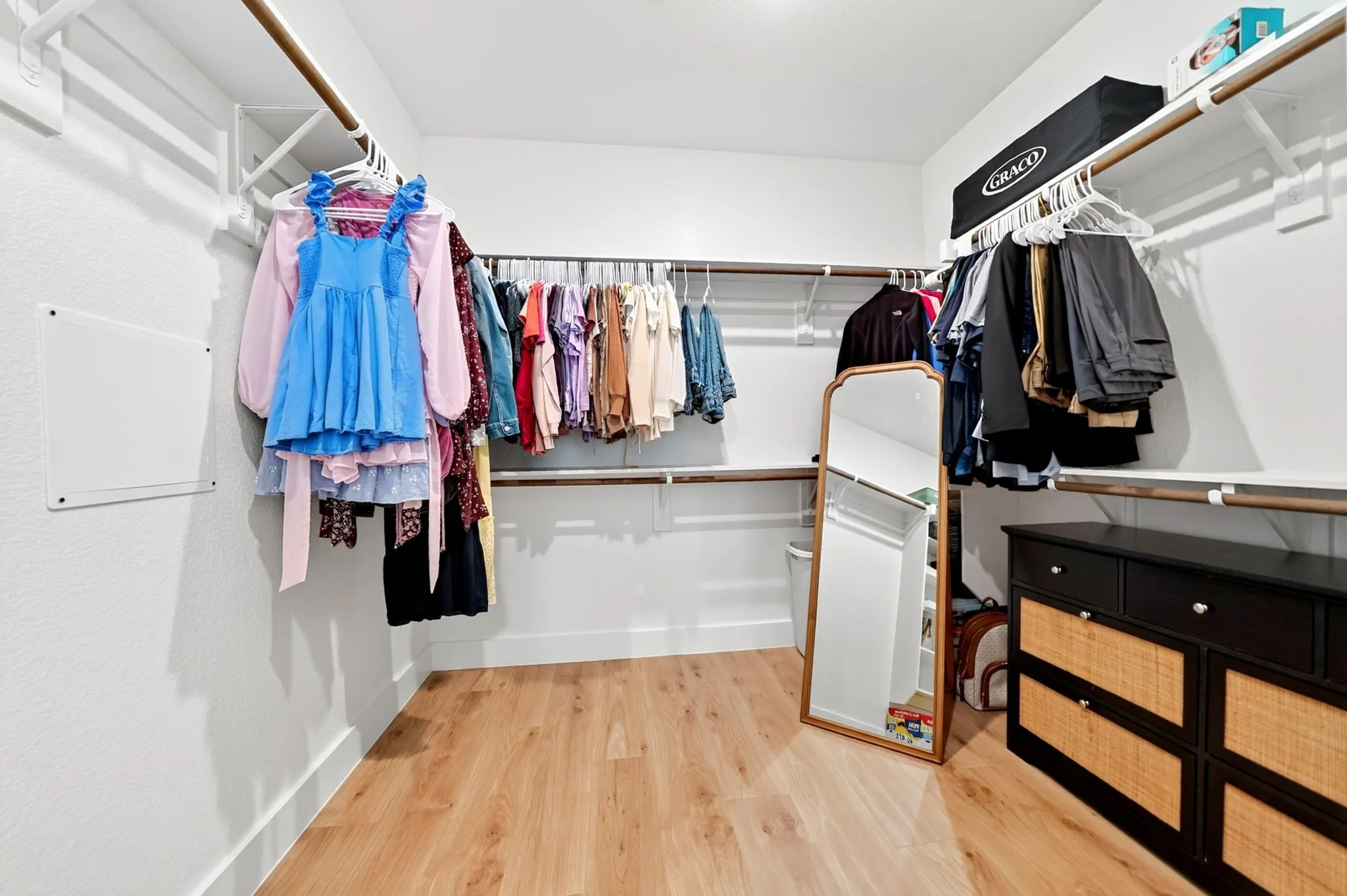 Walk-in closet featuring light wood-finish flooring, white walls, and multiple levels of shelving and hanging rods