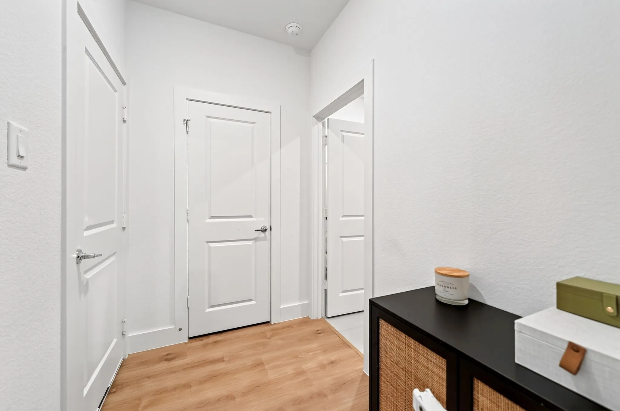 Hallway with wood-finish flooring, crisp white walls, and multiple paneled doors with chrome hardware
