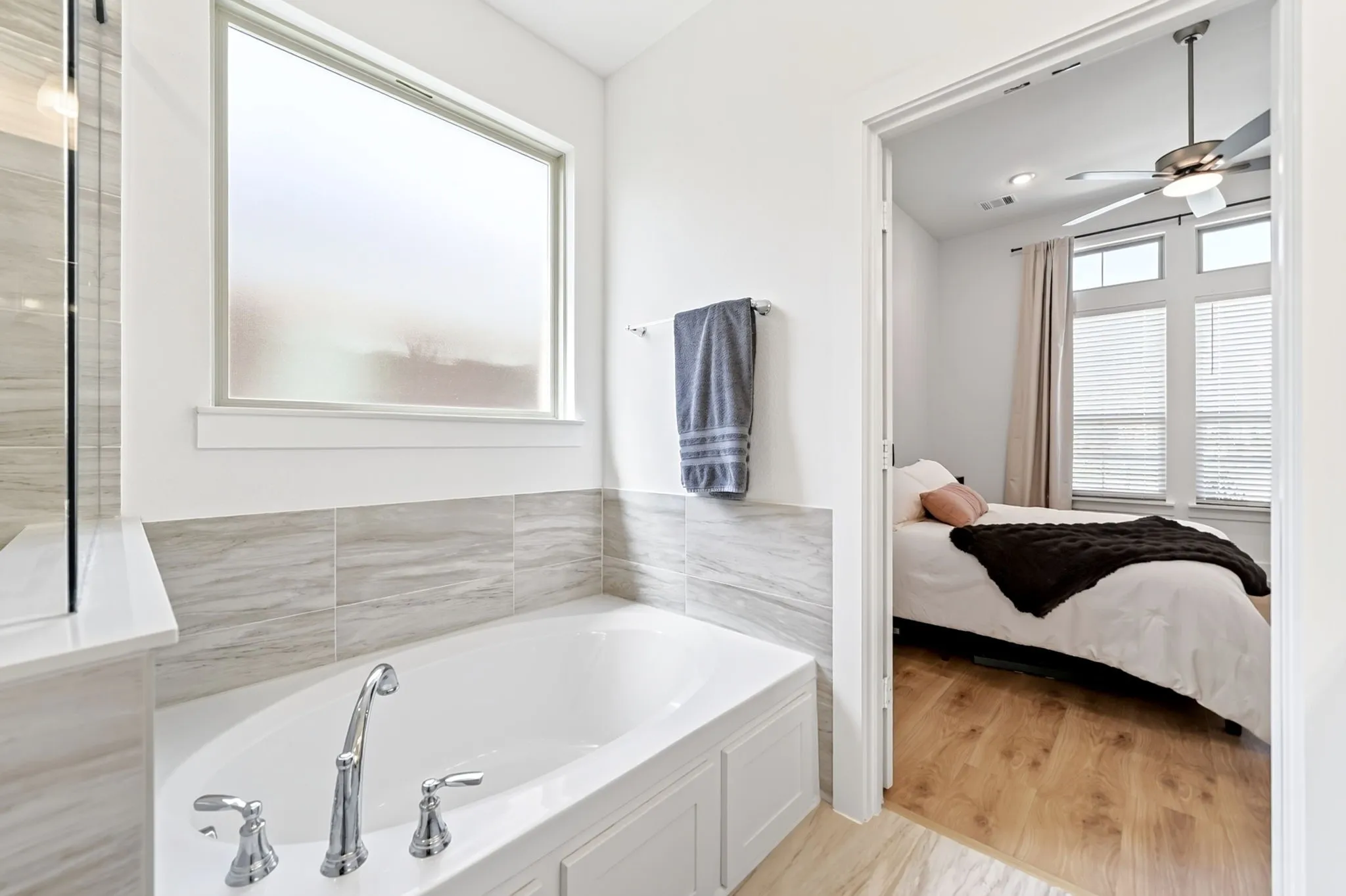 Soaking tub with chrome fixtures, surrounded by light-toned tile wainscoting and a frosted window