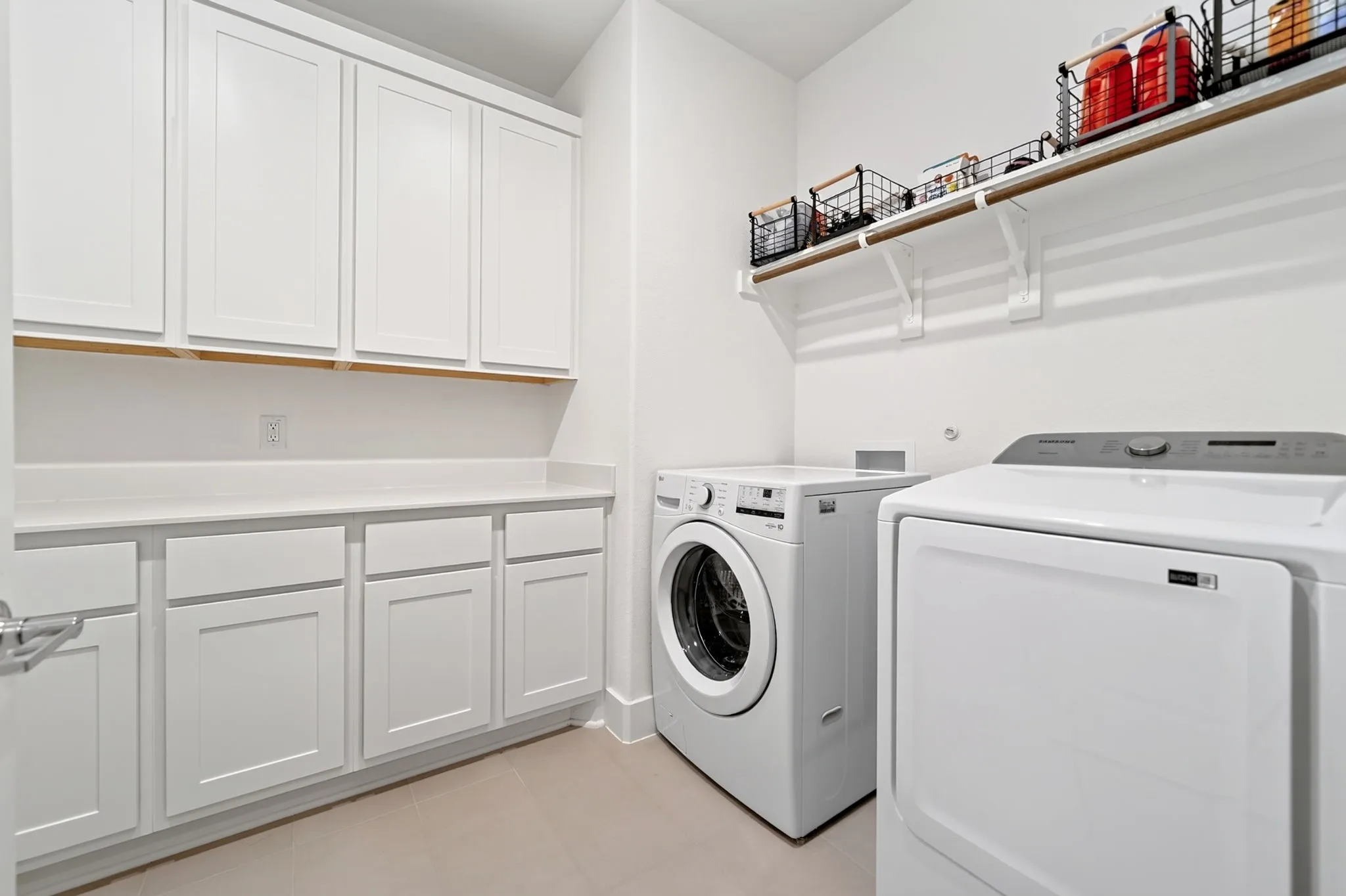 Laundry room featuring extensive white cabinetry, a light-toned countertop, open shelving with a wood-finish rod, and tile flooring