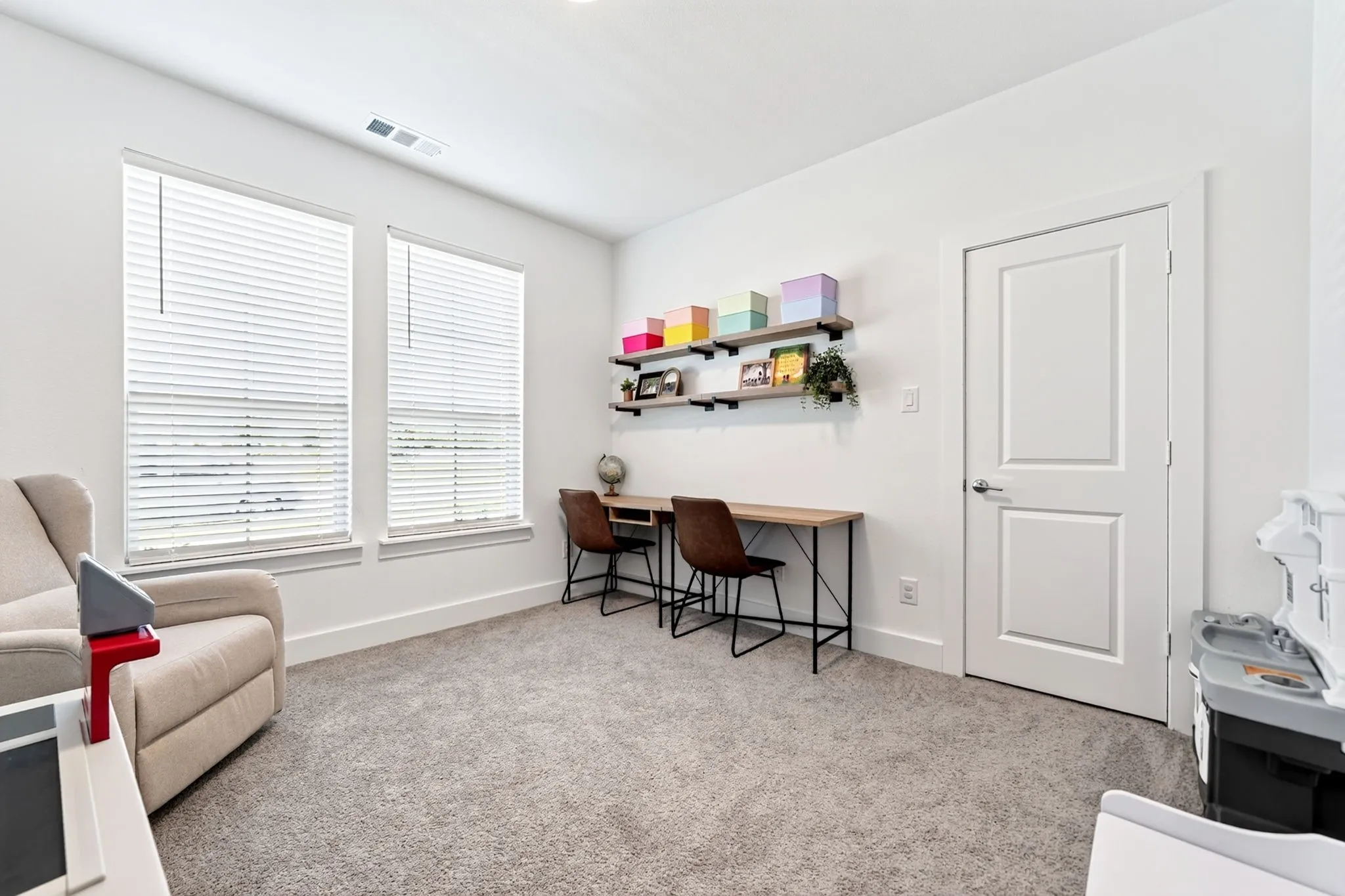 Bright room featuring two large windows with blinds, light gray carpet flooring, and a two-panel interior door with brushed nickel hardware