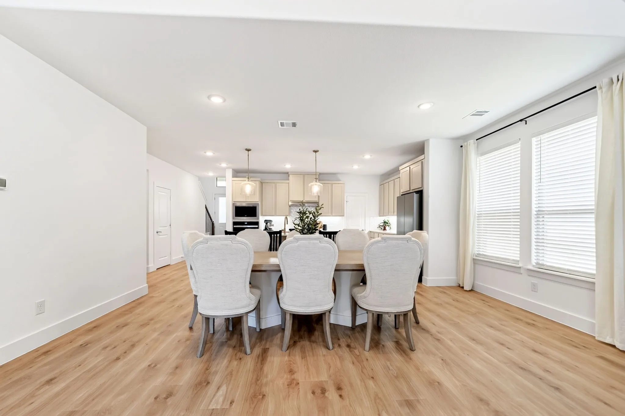 Open-concept dining area featuring wood-finish flooring, recessed lighting, and two large windows with blinds