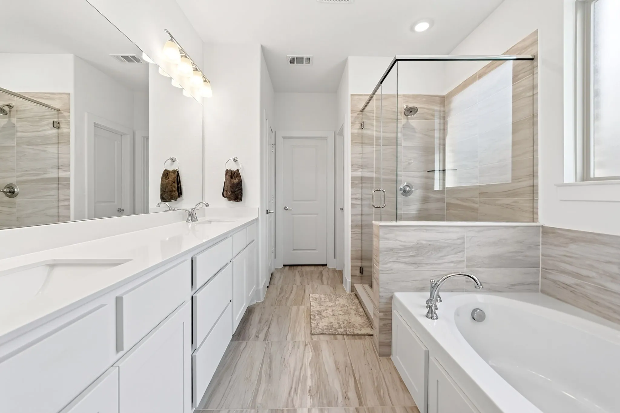 Spacious bathroom featuring a dual vanity with white cabinetry and countertops, a frameless glass shower enclosure, a built-in soaking tub, and wood-finish flooring
