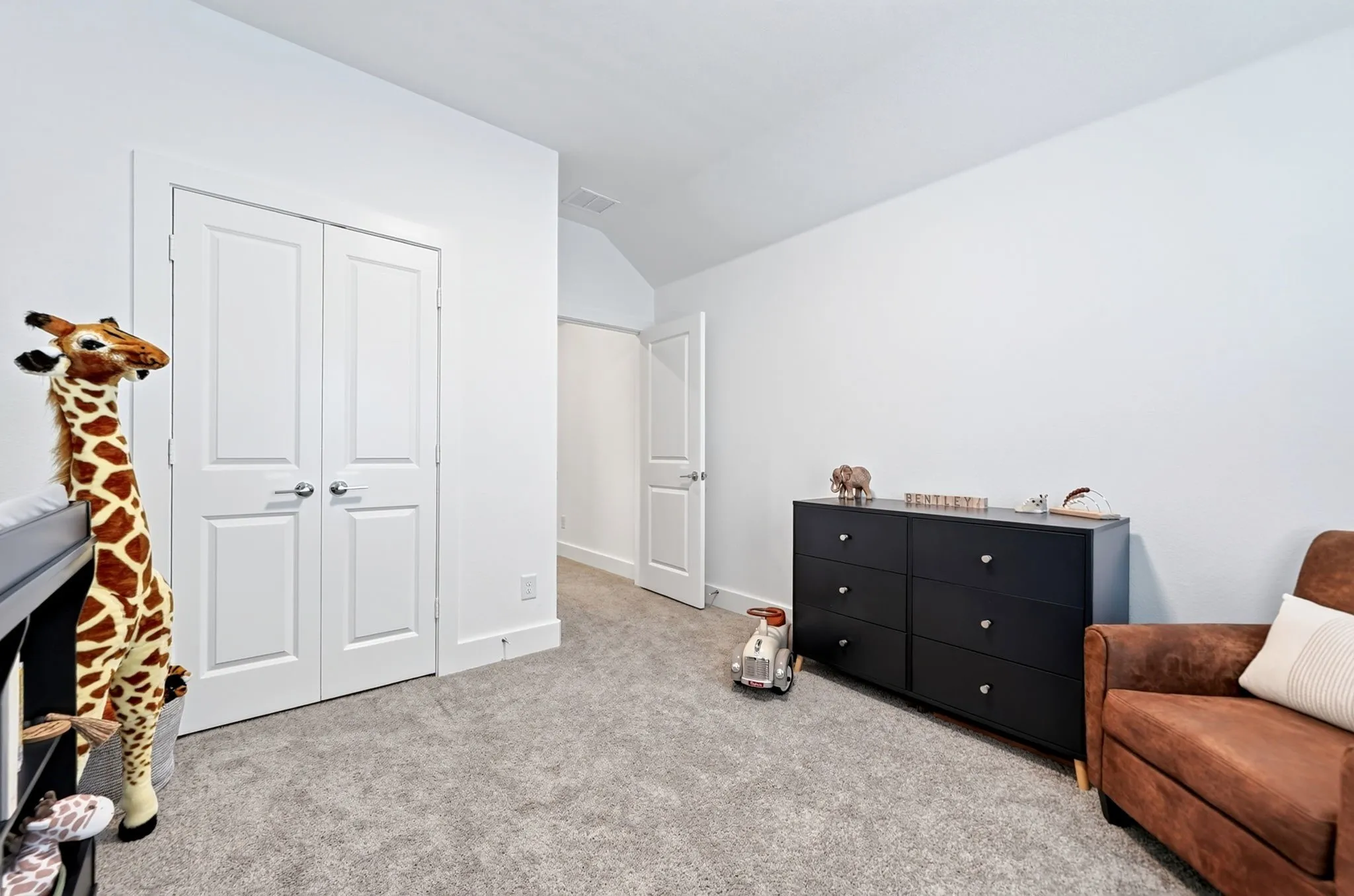 Light gray carpeted room with white walls, featuring a double-door closet with paneling and chrome hardware