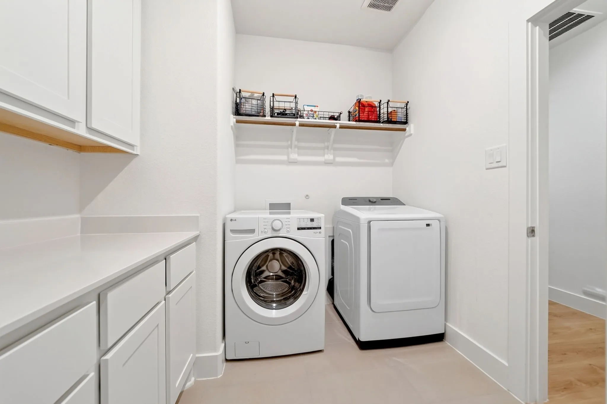 Laundry room featuring white shaker-style cabinetry, light-toned countertop, and open shelving