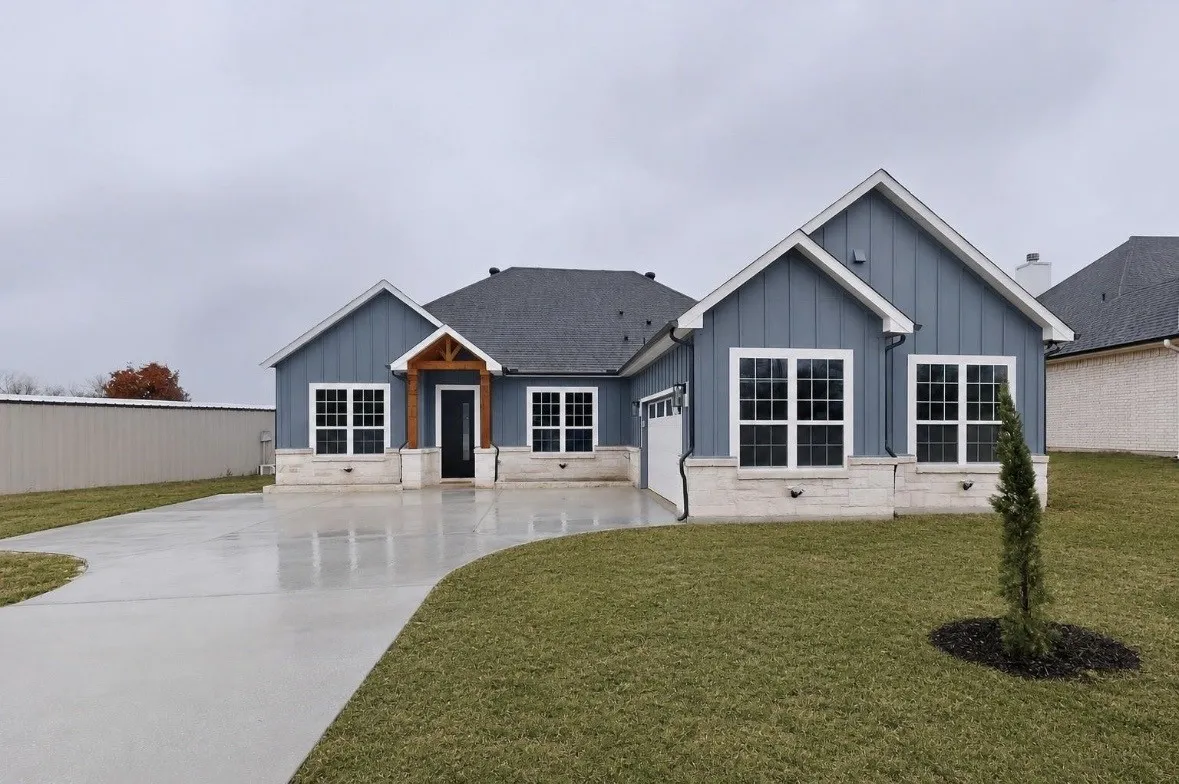 Contemporary exterior featuring blue board and batten siding, white window trim, stone accents, a dark roof, and a concrete driveway