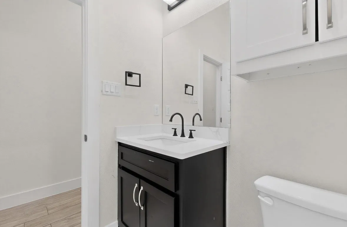 Modern vanity featuring a dark wood-finish cabinet with silver hardware, a white countertop, and a contemporary black faucet