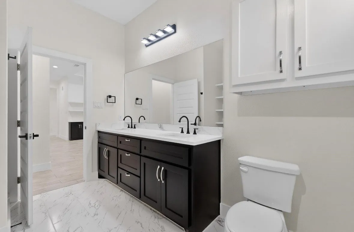 Bathroom featuring a dual vanity with dark wood cabinetry, white stone countertop, and matte black fixtures