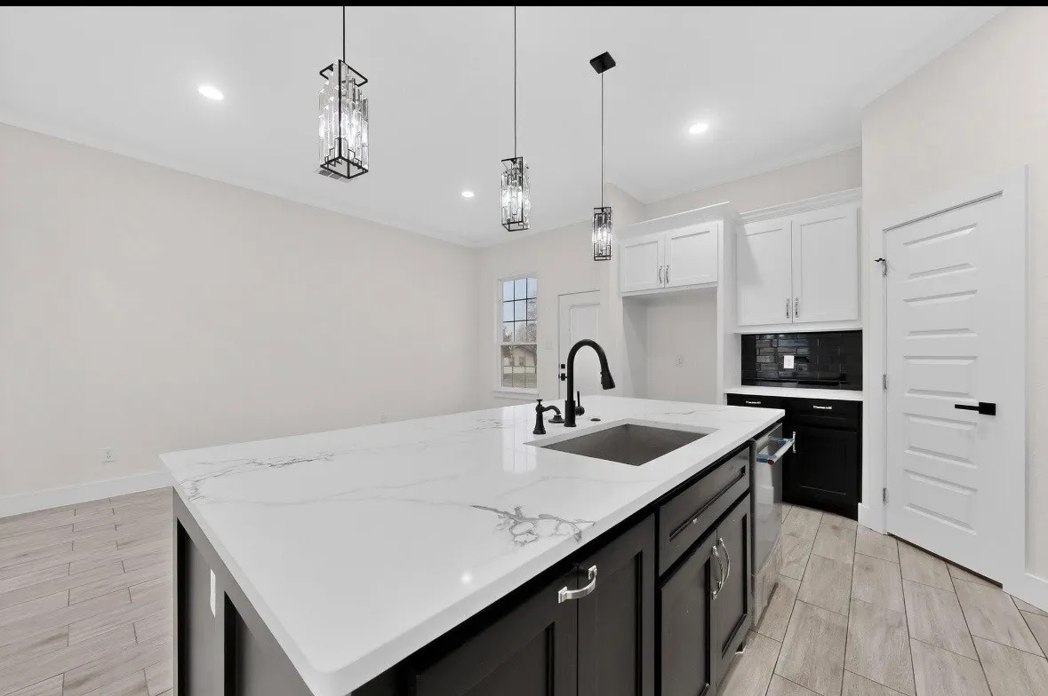 Kitchen island featuring a white countertop with grey veining, an undermount sink with a matte black faucet, and pendant lighting