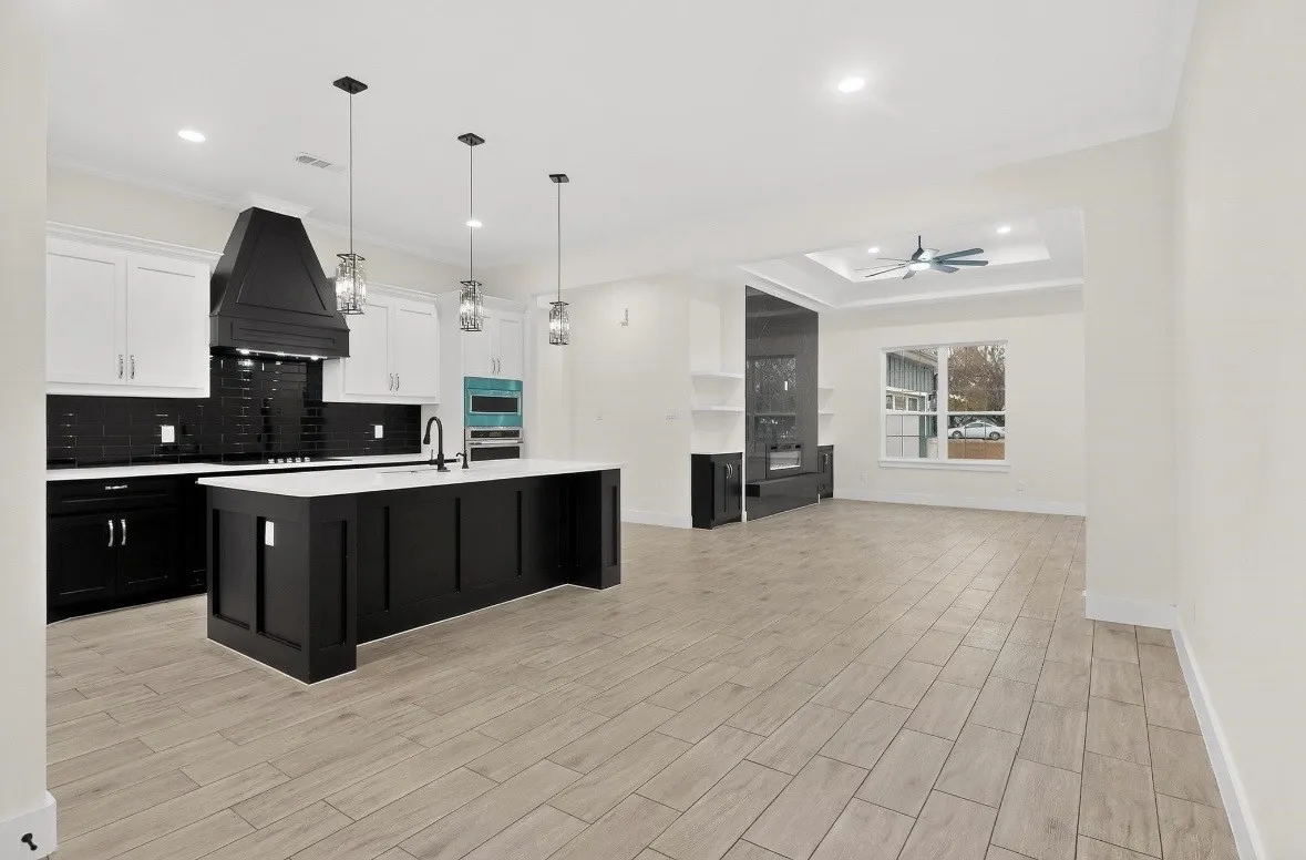 Open-concept living space featuring a gourmet kitchen with a large island, contrasting white and black cabinetry, and a black subway tile backsplash