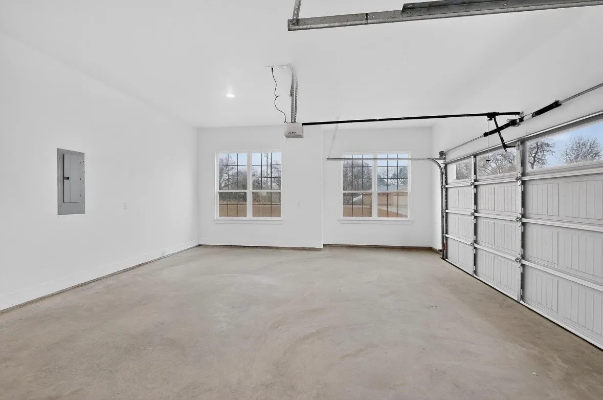 Spacious garage featuring a concrete floor, two windows, and an overhead door with an automatic opener