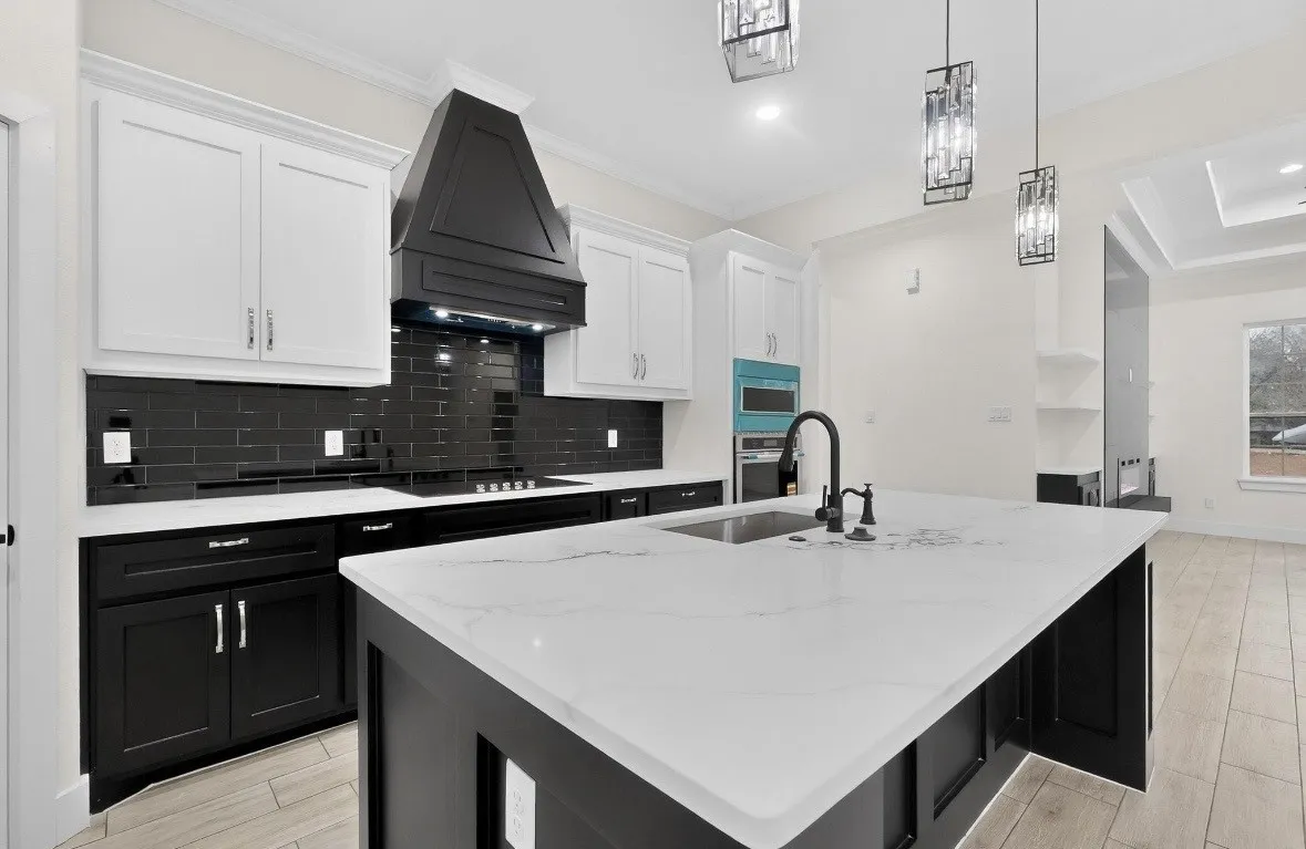 Kitchen featuring a large island with an undermount sink, white countertops, black and white cabinetry, a black subway tile backsplash, and tile flooring