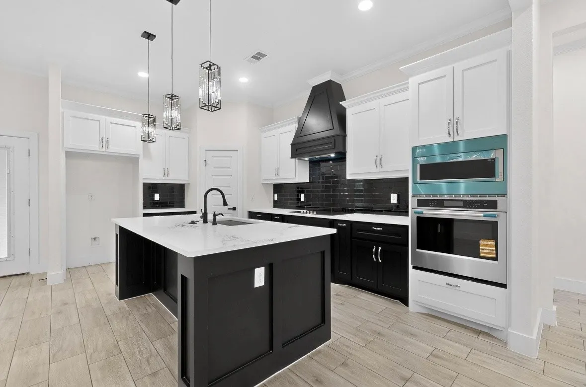 Kitchen featuring a dark-toned island with an integrated sink and black faucet, white shaker-style perimeter cabinetry, black subway tile backsplash, and light wood-finish flooring