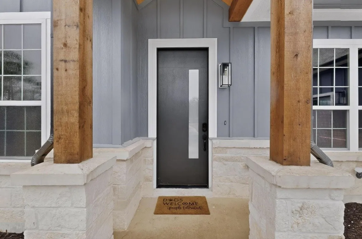 Modern black entry door with vertical glass accent, framed by board and batten siding, stone facade, and substantial wood-finish posts