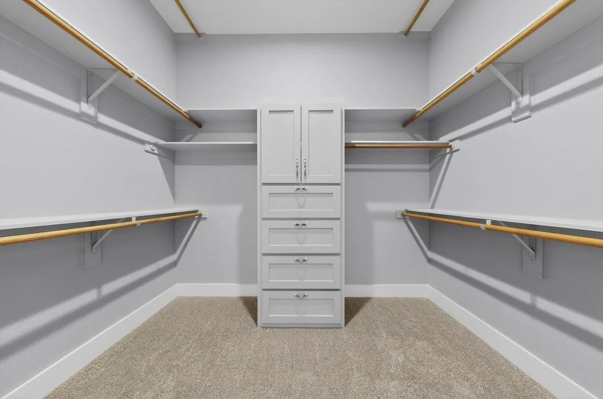 Spacious walk-in closet featuring extensive built-in shelving, hanging rods, central cabinetry with drawers, and light-toned carpeting