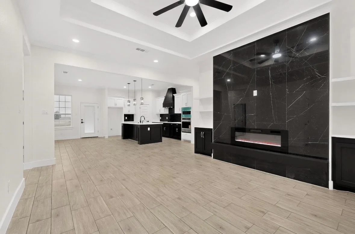Spacious living area featuring light wood-finish flooring, a tray ceiling with a ceiling fan, and recessed lighting