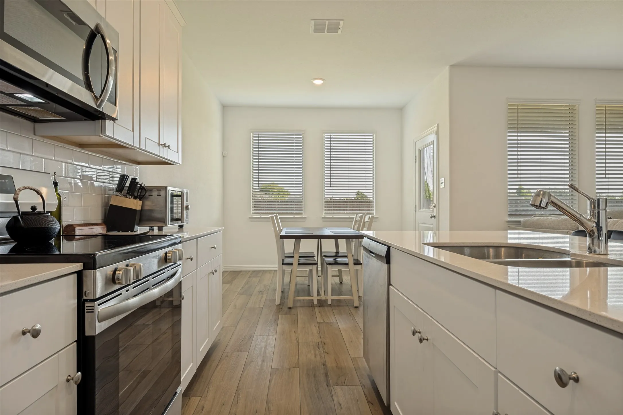 Modern kitchen featuring white cabinetry, stainless steel appliances, light-toned countertops, subway tile backsplash, and wood-finish flooring