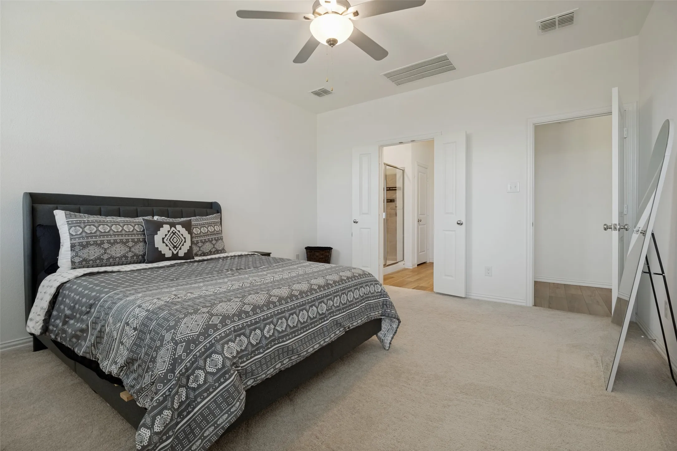 Carpeted room featuring a ceiling fan with integrated lighting, white walls, and a doorway leading to a bathroom with wood-finish flooring and a glass-enclosed shower