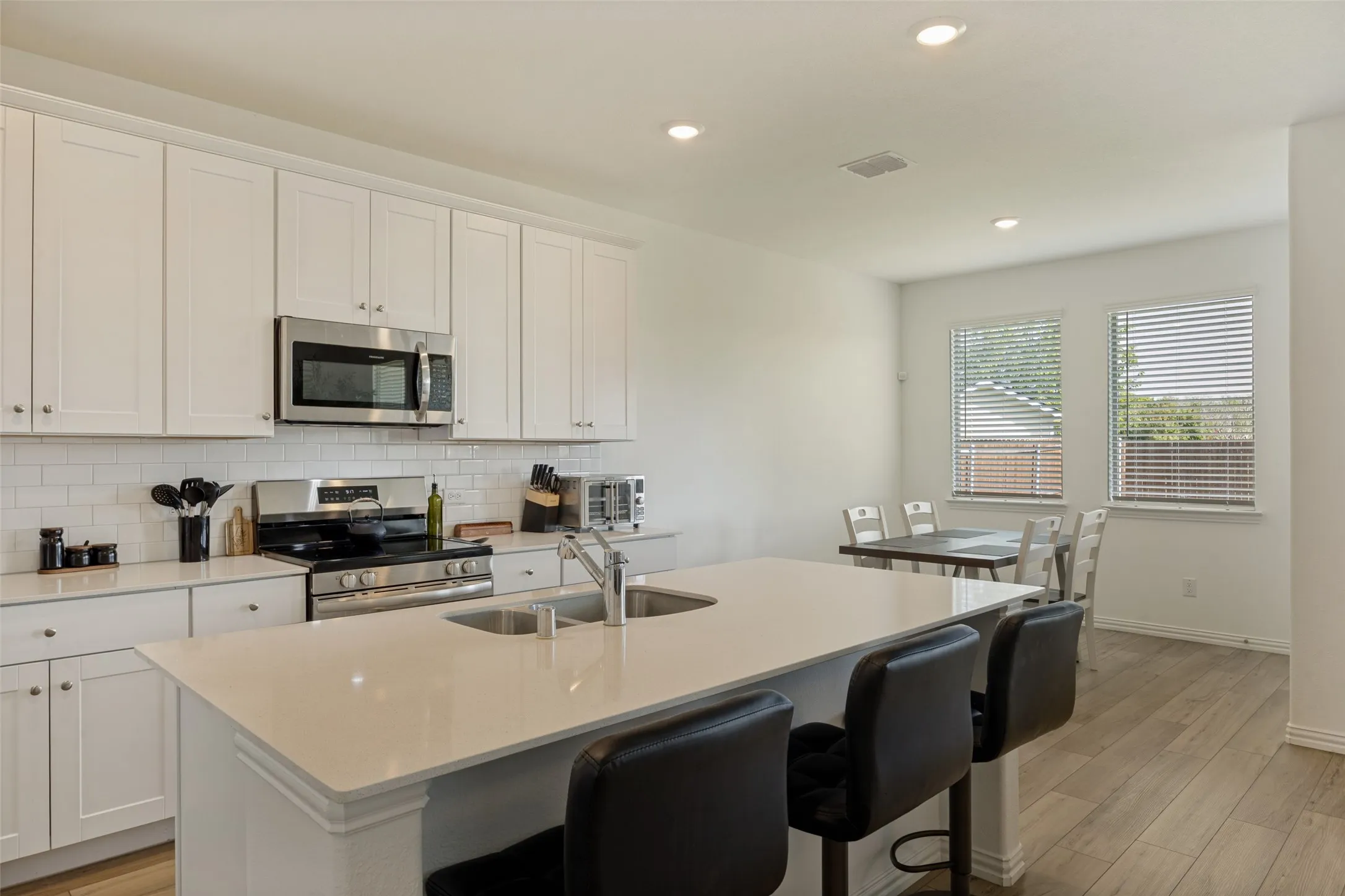 Kitchen featuring a large island with dual sinks, stainless steel appliances, white subway tile backsplash, white cabinetry, and wood-finish flooring