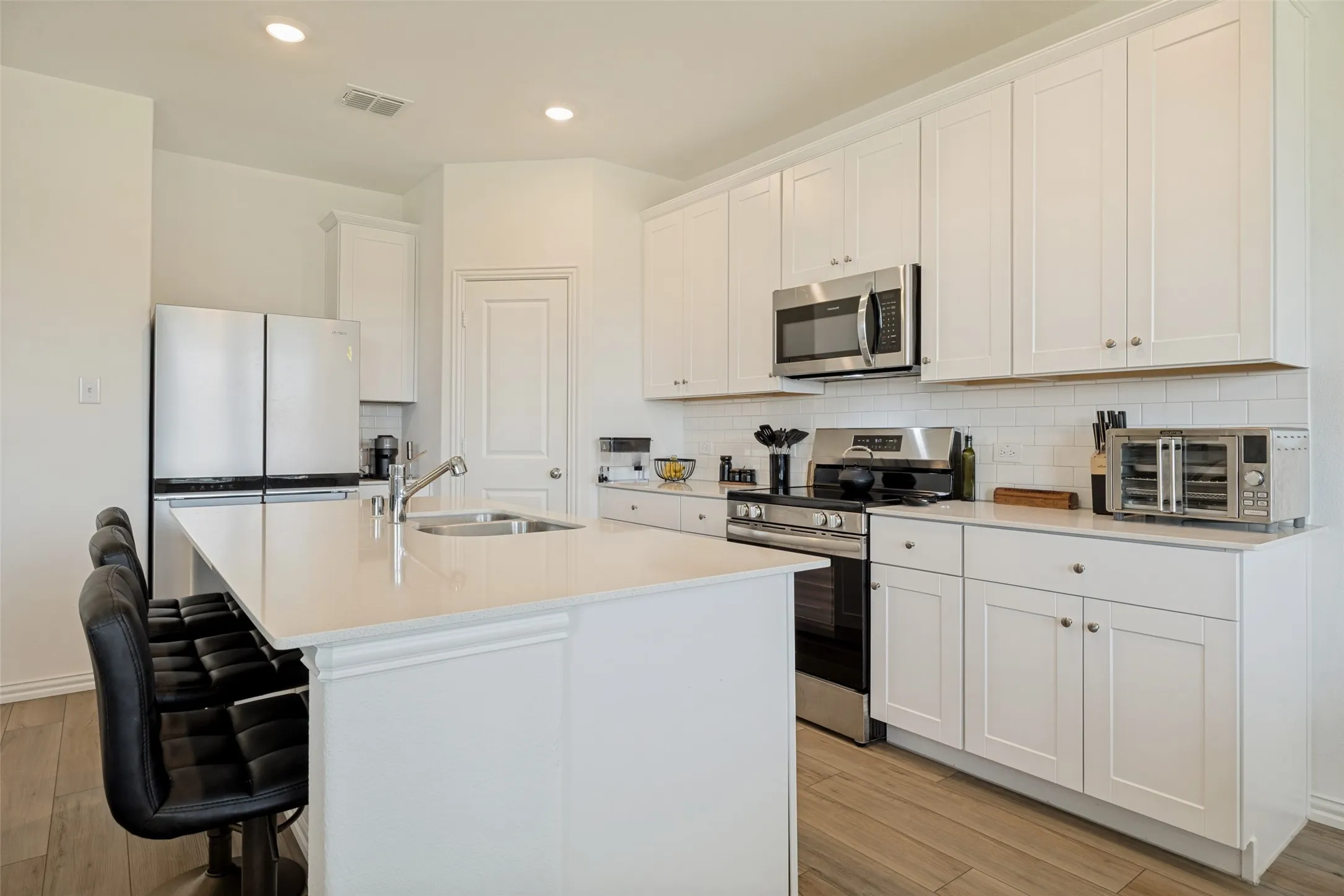 Modern kitchen featuring white shaker cabinetry, stainless steel appliances, a center island with sink, subway tile backsplash, and wood-finish flooring