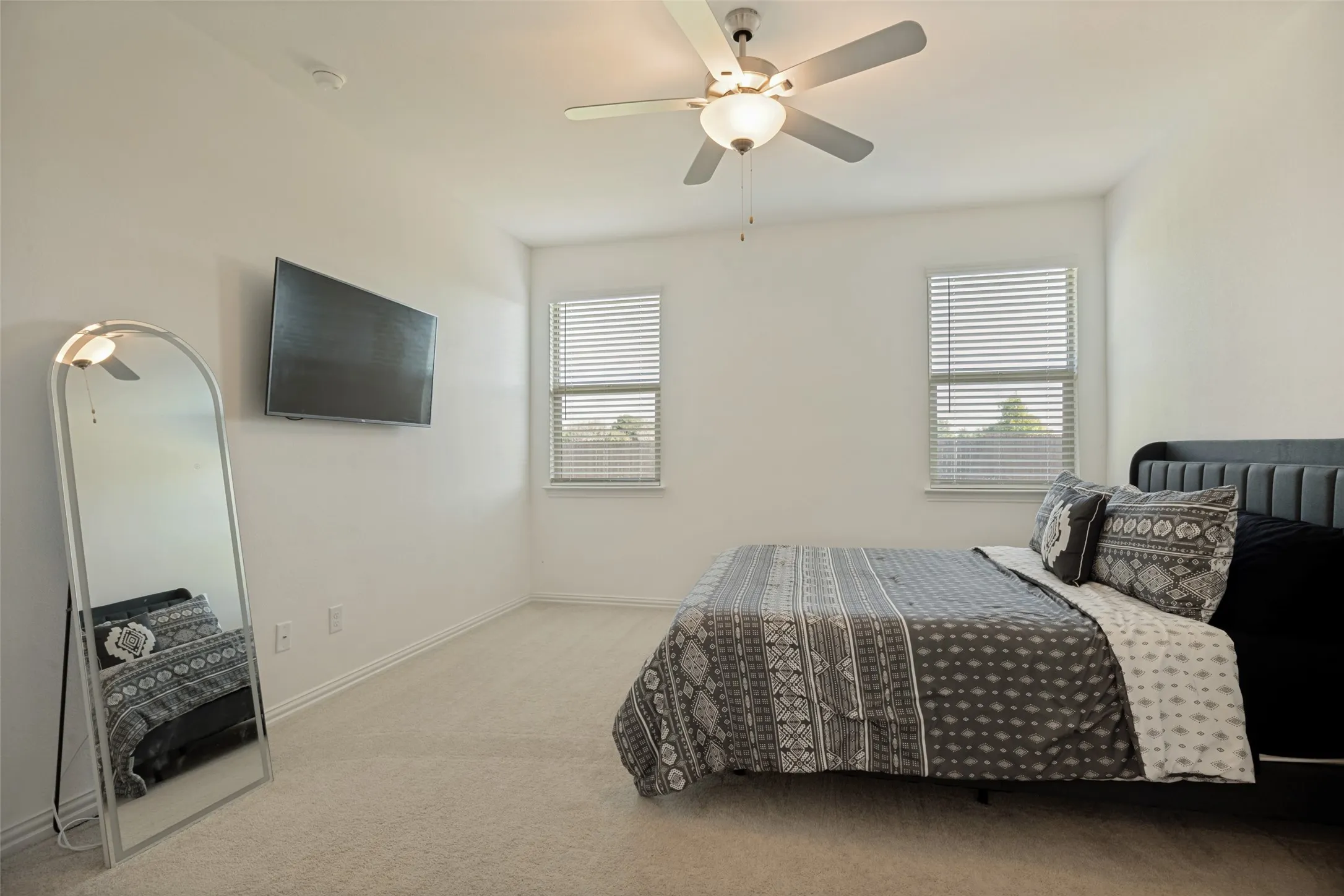 Bright bedroom featuring light-colored carpeting, white walls, two windows with blinds, and a ceiling fan with integrated lighting