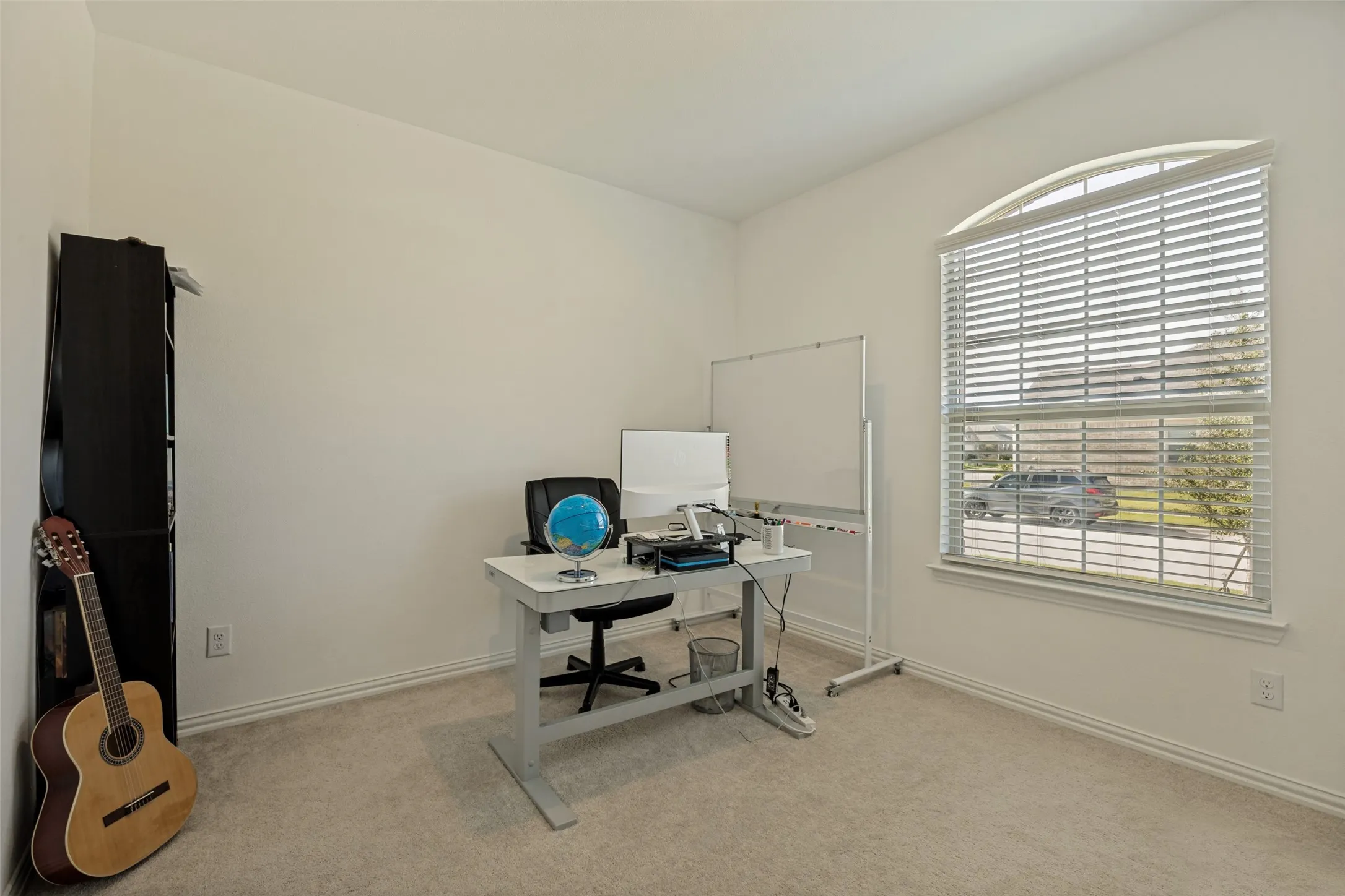 Room featuring an arched window with blinds, light-colored carpeting, and neutral painted walls