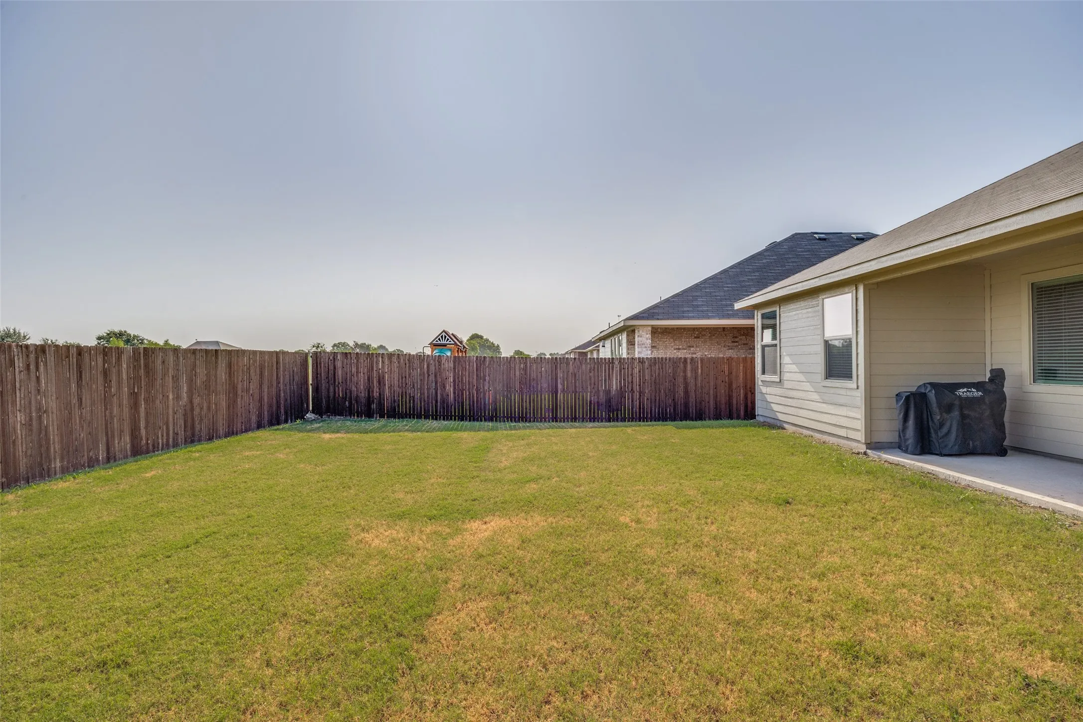 Expansive backyard featuring a lush lawn, privacy fencing, and a concrete patio